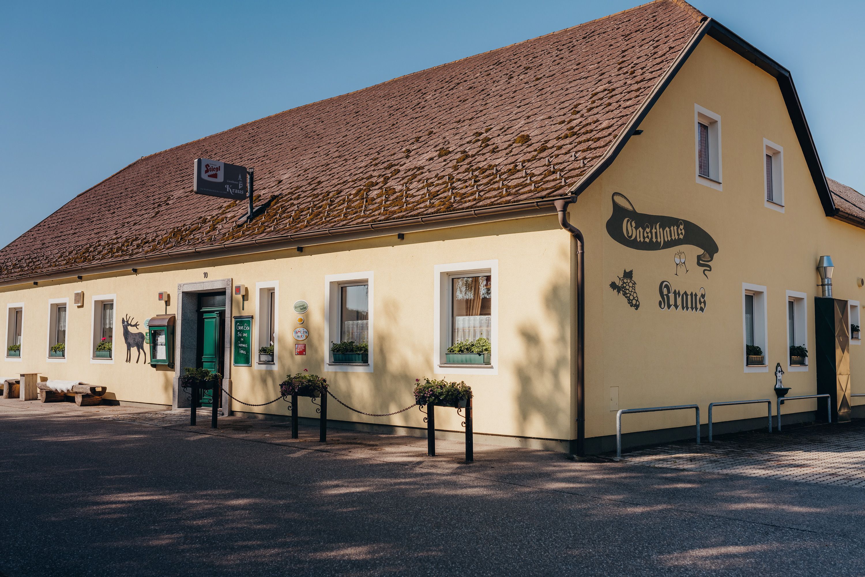 Gelbes Gasthaus mit braunem Dach und grüner Tür, beschriftet mit 'Gasthaus Kraus'.