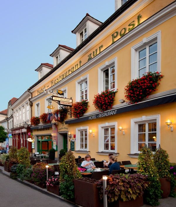 Fassade eines gelben Gebäudes mit dem Schriftzug 'Hotel-Restaurant zur Post'. Vor dem Gebäude sitzen Menschen an Tischen.