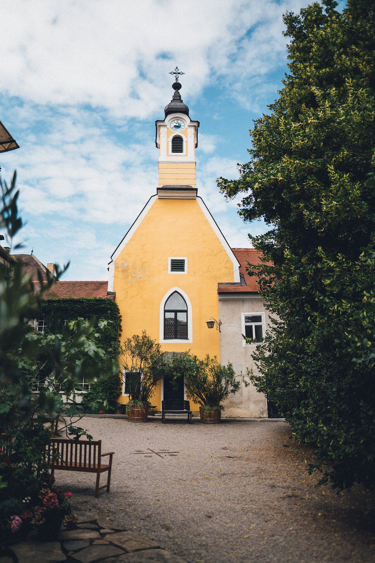 Die strahlend gelbe Fassade des Nikolaihofs zieht die Blicke auf sich und strahlt eine einladende Atmosphäre aus. Umgeben von üppigem Grün und blühenden Pflanzen, bietet dieser Ort eine perfekte Kulisse für Weinliebhaber und Naturliebhaber gleichermaßen. Hier, wo die Donau sanft fließt, erleben Besucher die Harmonie von Tradition und Natur.