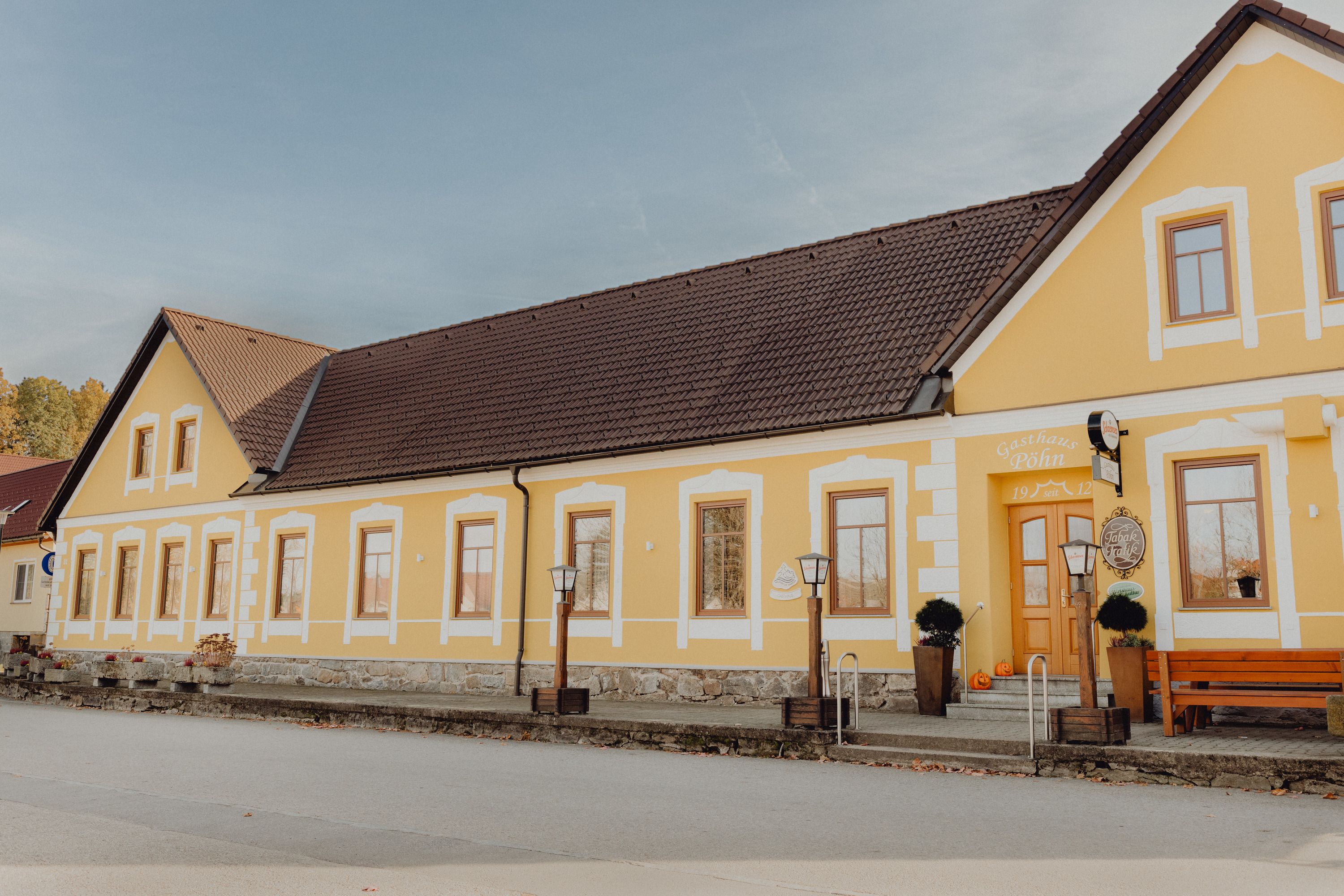 Gelbes Wirtshaus mit braunem Dach und mehreren Fenstern, dekoriert mit Kürbissen vor dem Eingang.