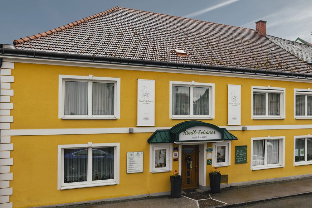 Gelbes Gasthaus mit grüner Markise und mehreren Fenstern.