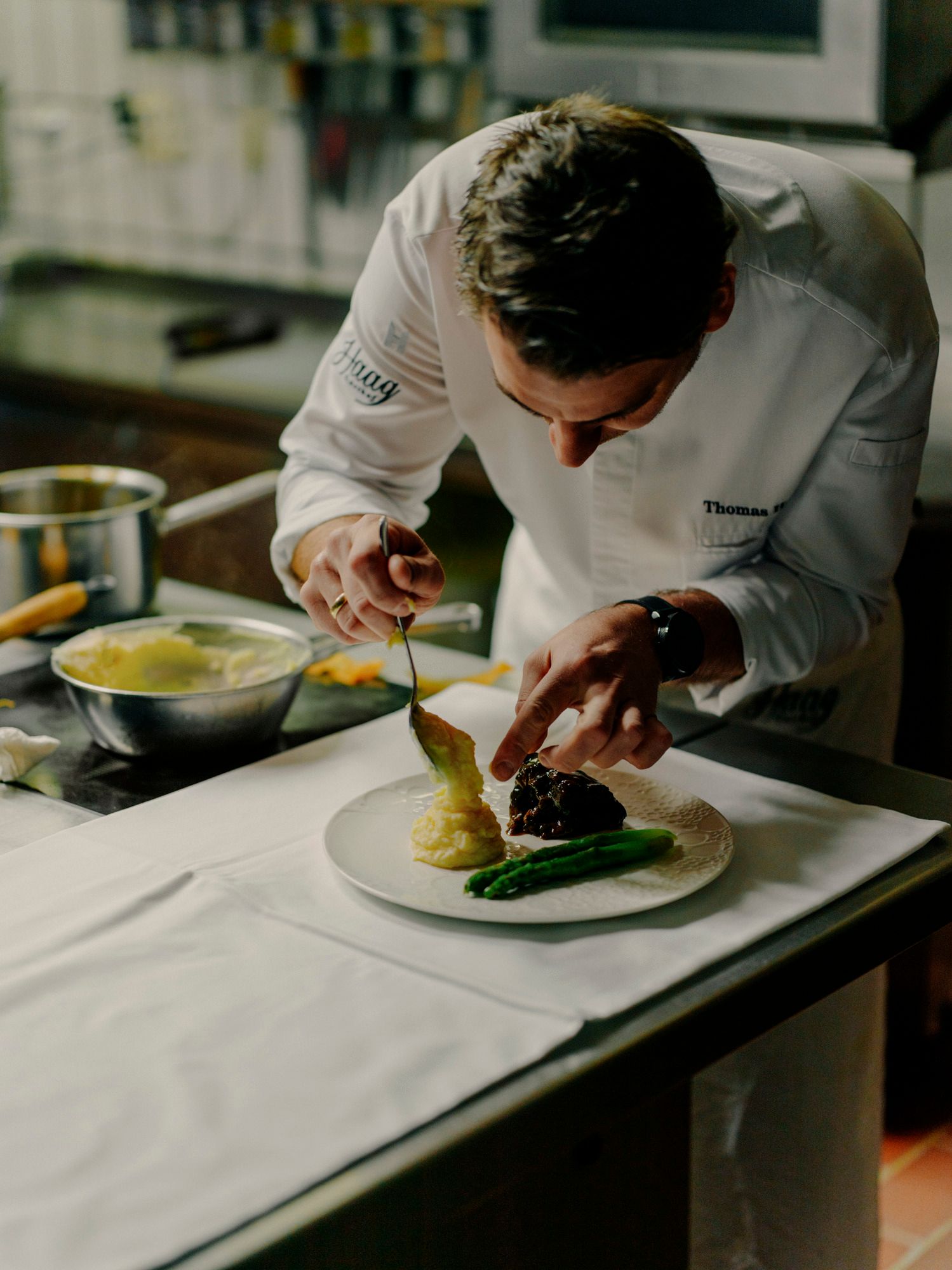 Ein Koch richtet ein Gericht mit Spargel und Kartoffelpüree auf einem Teller an.