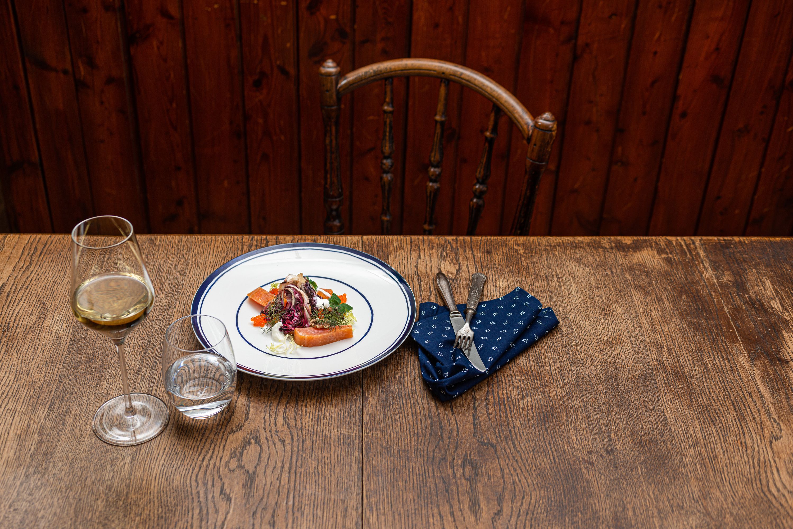 Weißer Teller mit Bratapfel und Lachsforelle auf Holztisch.