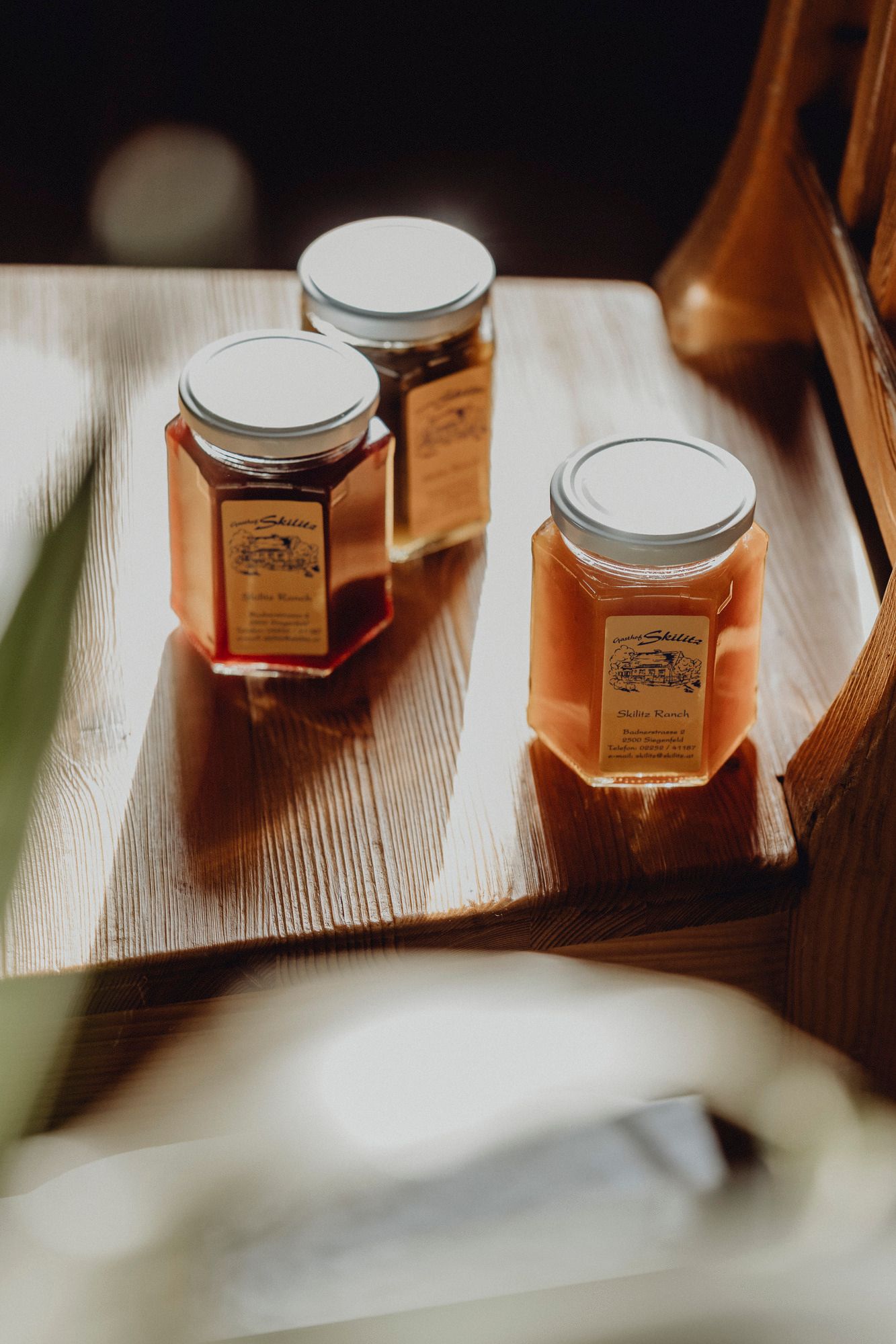 Drei Gläser mit Marmelade auf einem Holztisch, beschriftet mit 'Skilitz Ranch'.
