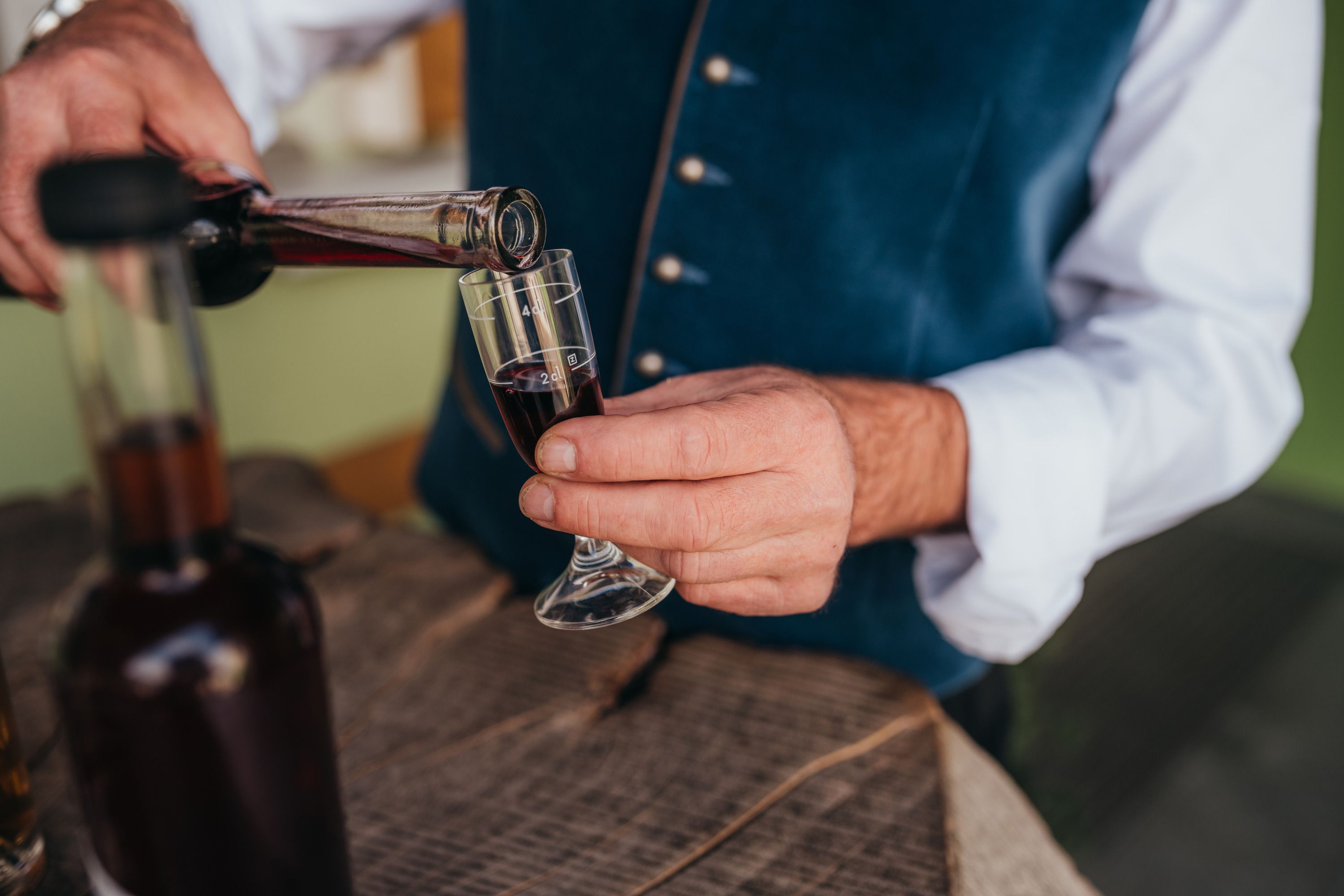 Person gießt roten Likör in ein kleines Glas.