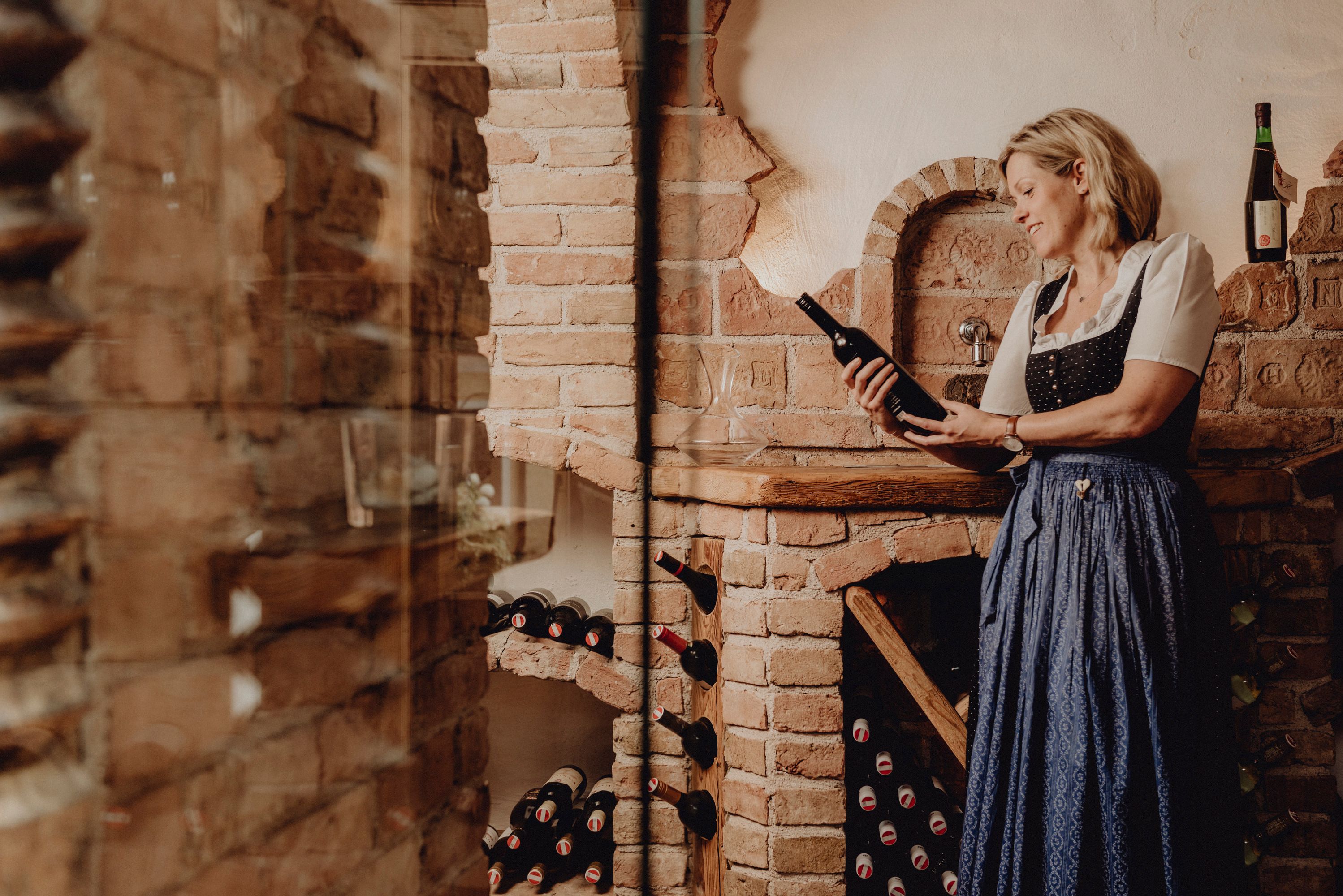 Frau in traditioneller Kleidung hält eine Weinflasche in einem rustikalen Weinkeller.