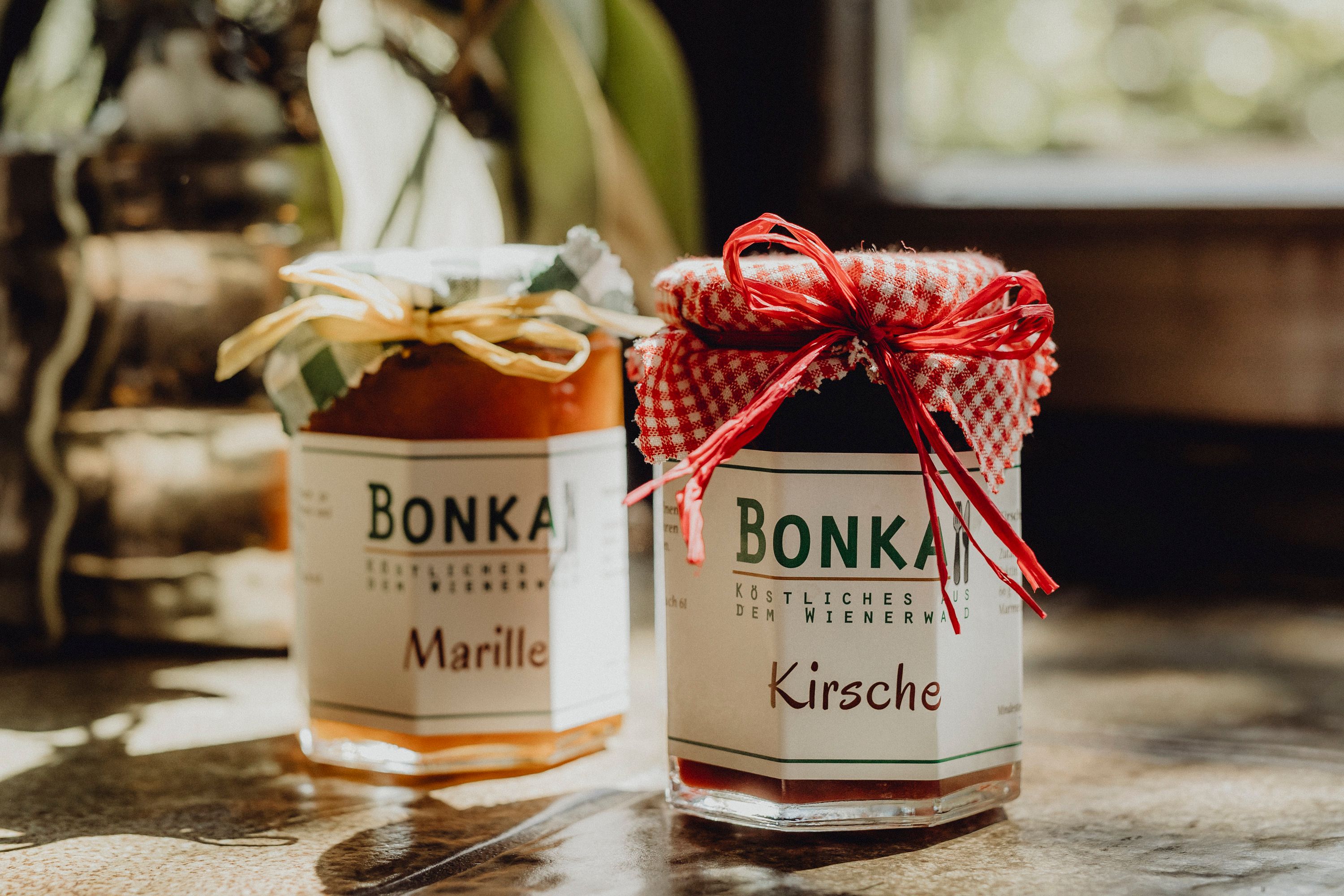 Zwei Gläser Marmelade mit Etiketten 'Bonka', eins mit Marille, das andere mit Kirsche, auf einem Tisch.