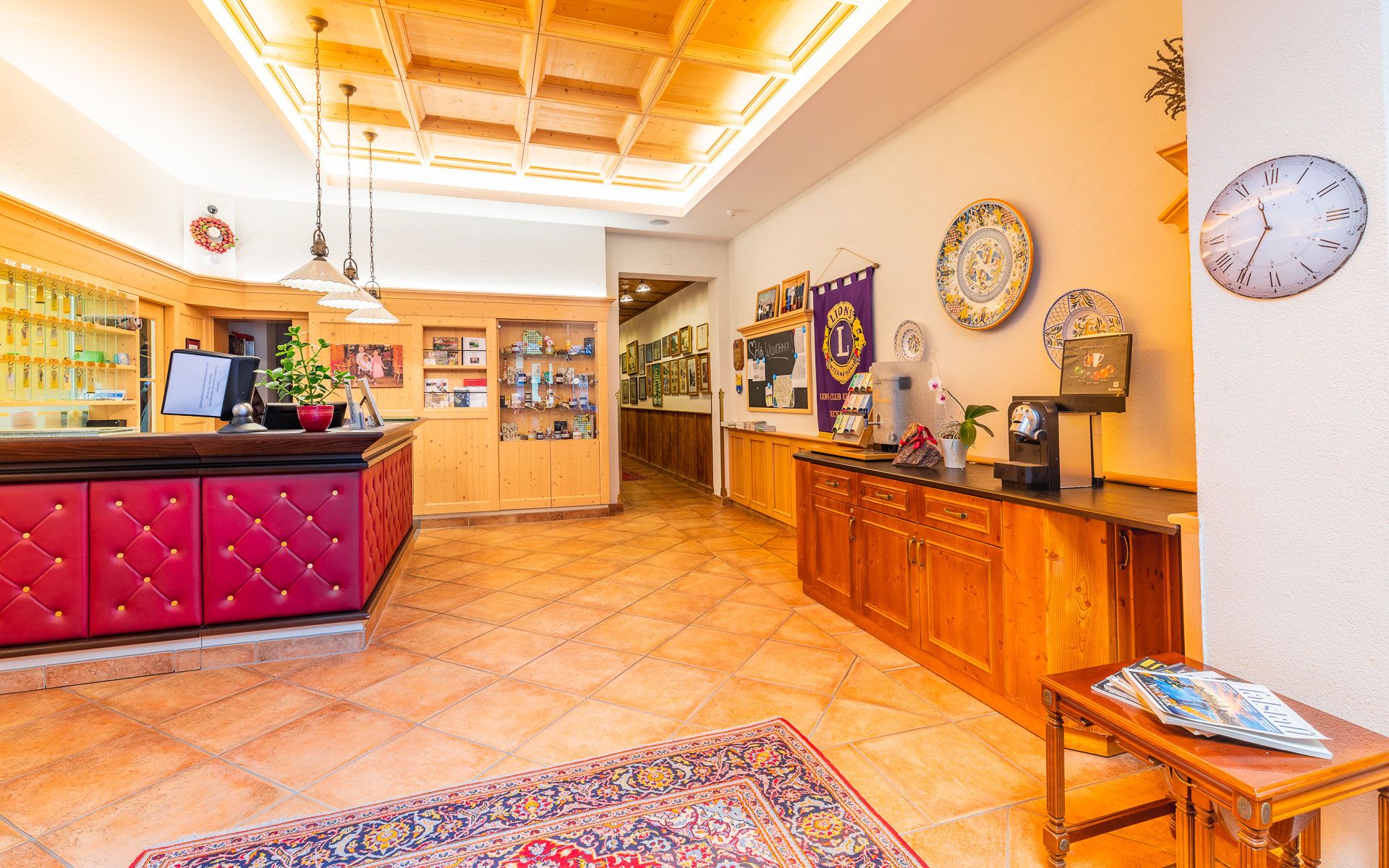 Empfangsbereich mit Holzmöbeln, rotem Tresen, dekorativen Tellern an der Wand und einer Uhr.