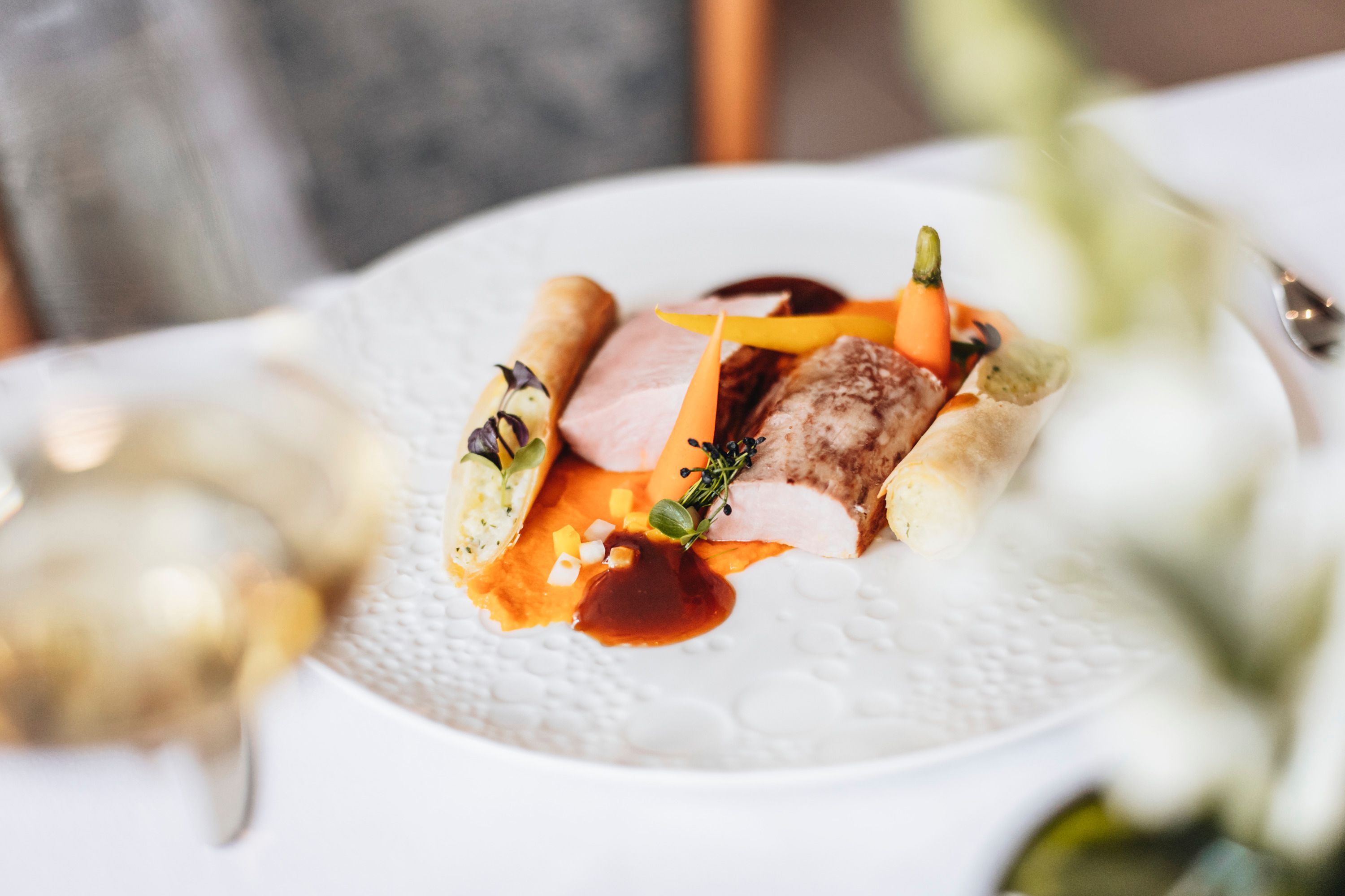 Gourmetgericht mit Schweinefilet, Gemüse und Kartoffelrolle auf einem weißen Teller.