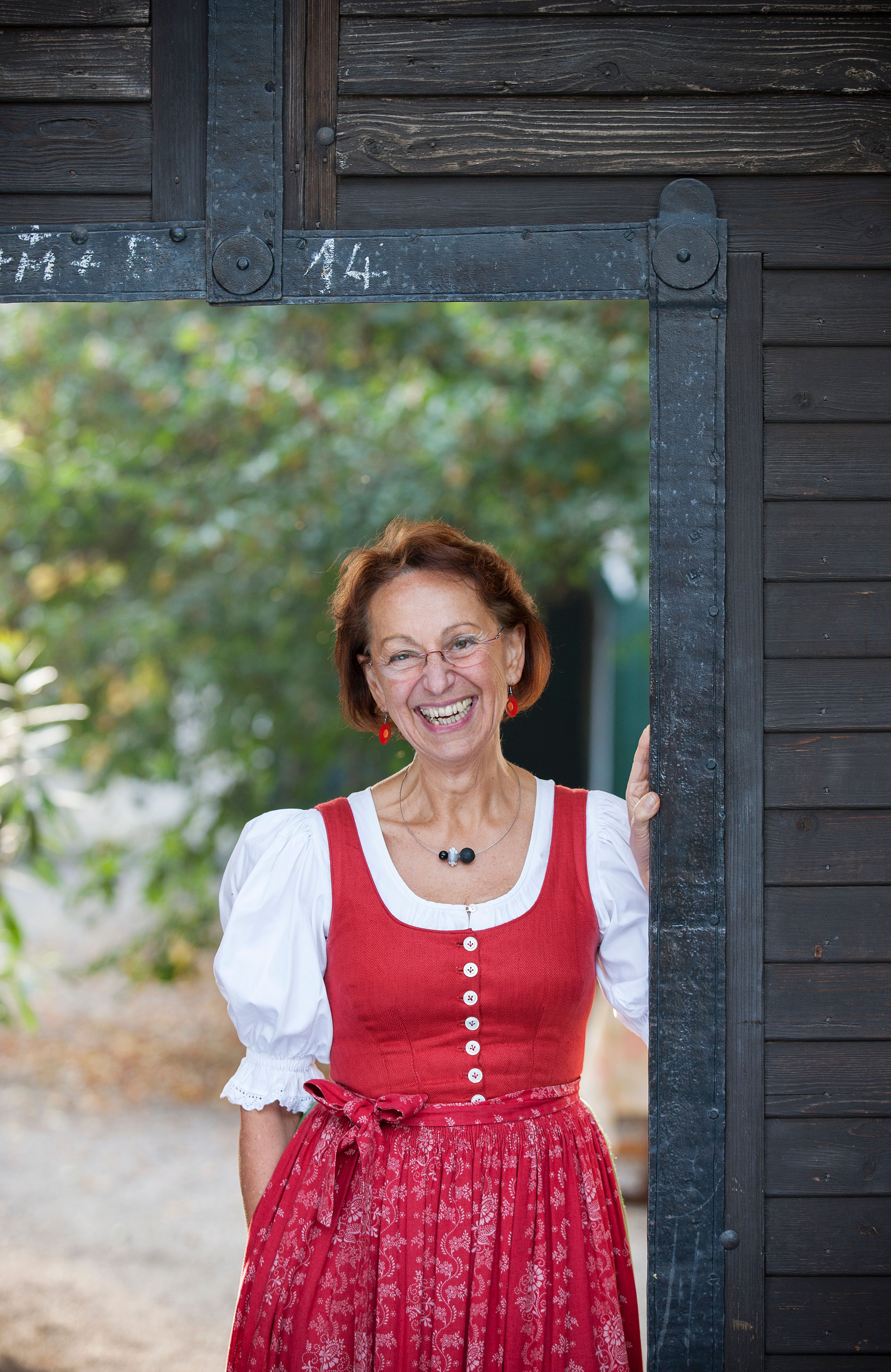Eine Frau in traditioneller Tracht steht lächelnd in einem Türrahmen aus Holz.