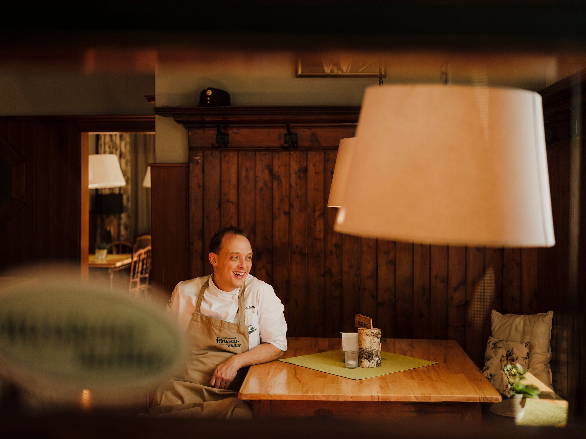 In einem einladenden Wirtshaus, umgeben von rustikalem Holz, strahlt der Wirt Patrick Friedrich eine herzliche Gastfreundschaft aus. Die Atmosphäre ist geprägt von der Gemütlichkeit des ländlichen Lebens, während die sanften Klänge des Donauflusses im Hintergrund eine entspannende Stimmung schaffen.