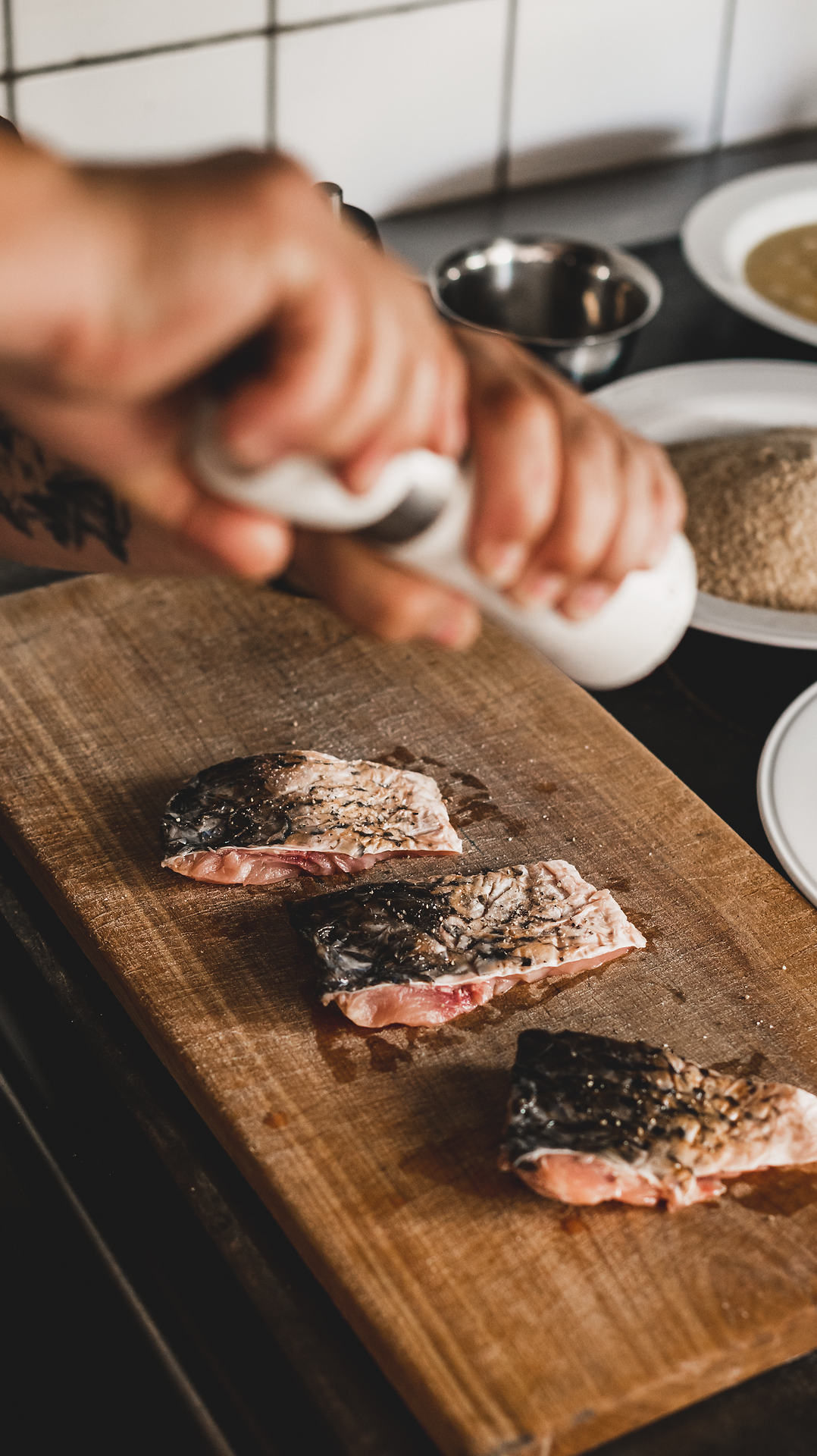 Frisch zubereitete Teichkarpfenstücke liegen appetitlich auf einem Holzbrett, während ein Koch mit Hingabe Gewürze hinzufügt. Die Atmosphäre ist geprägt von der rustikalen Gemütlichkeit des Gasthofs, wo regionale Köstlichkeiten im Mittelpunkt stehen.
