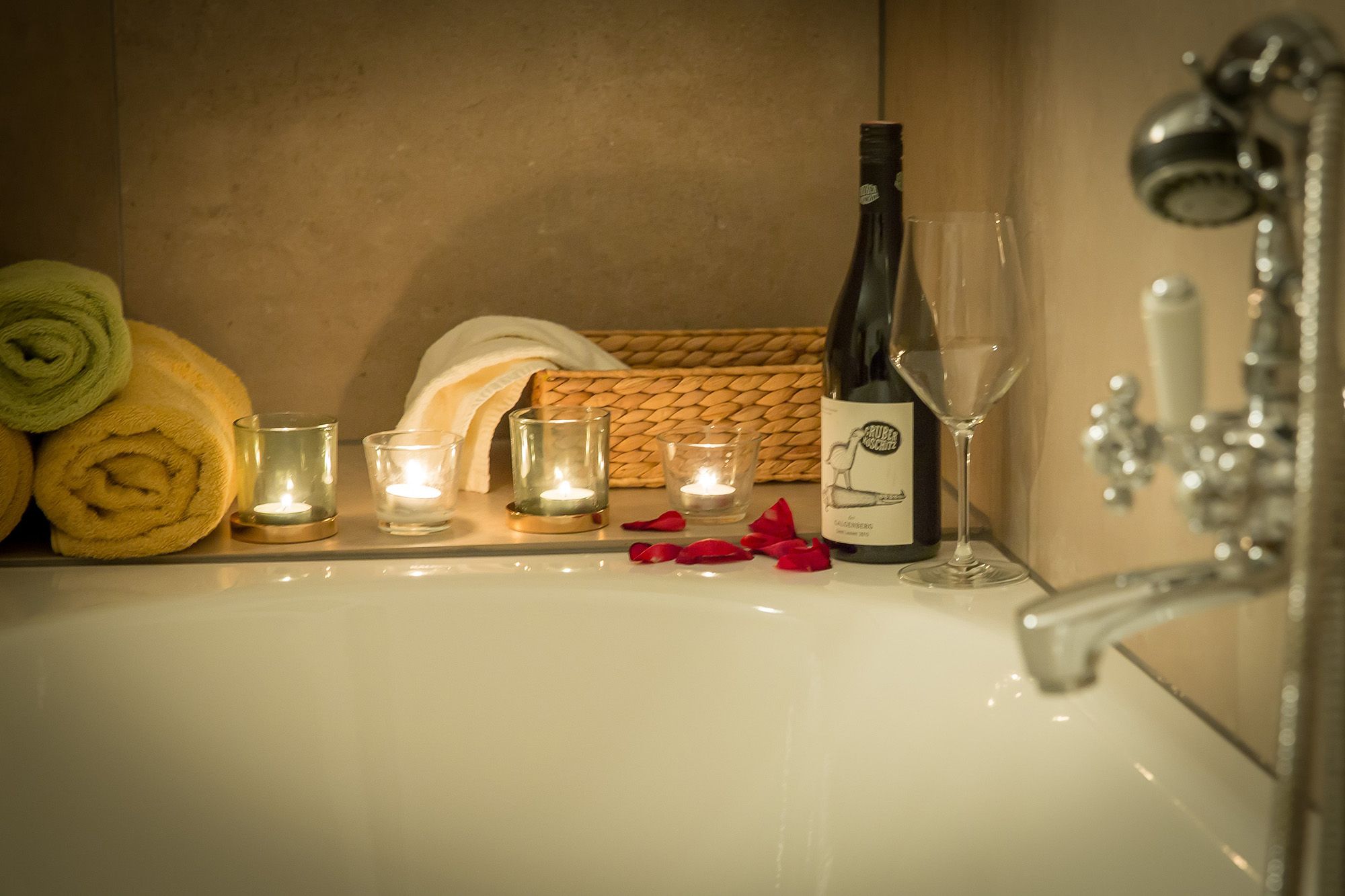 Romantisches Badezimmer mit Kerzen, Weinflasche und Rosenblättern am Badewannenrand.