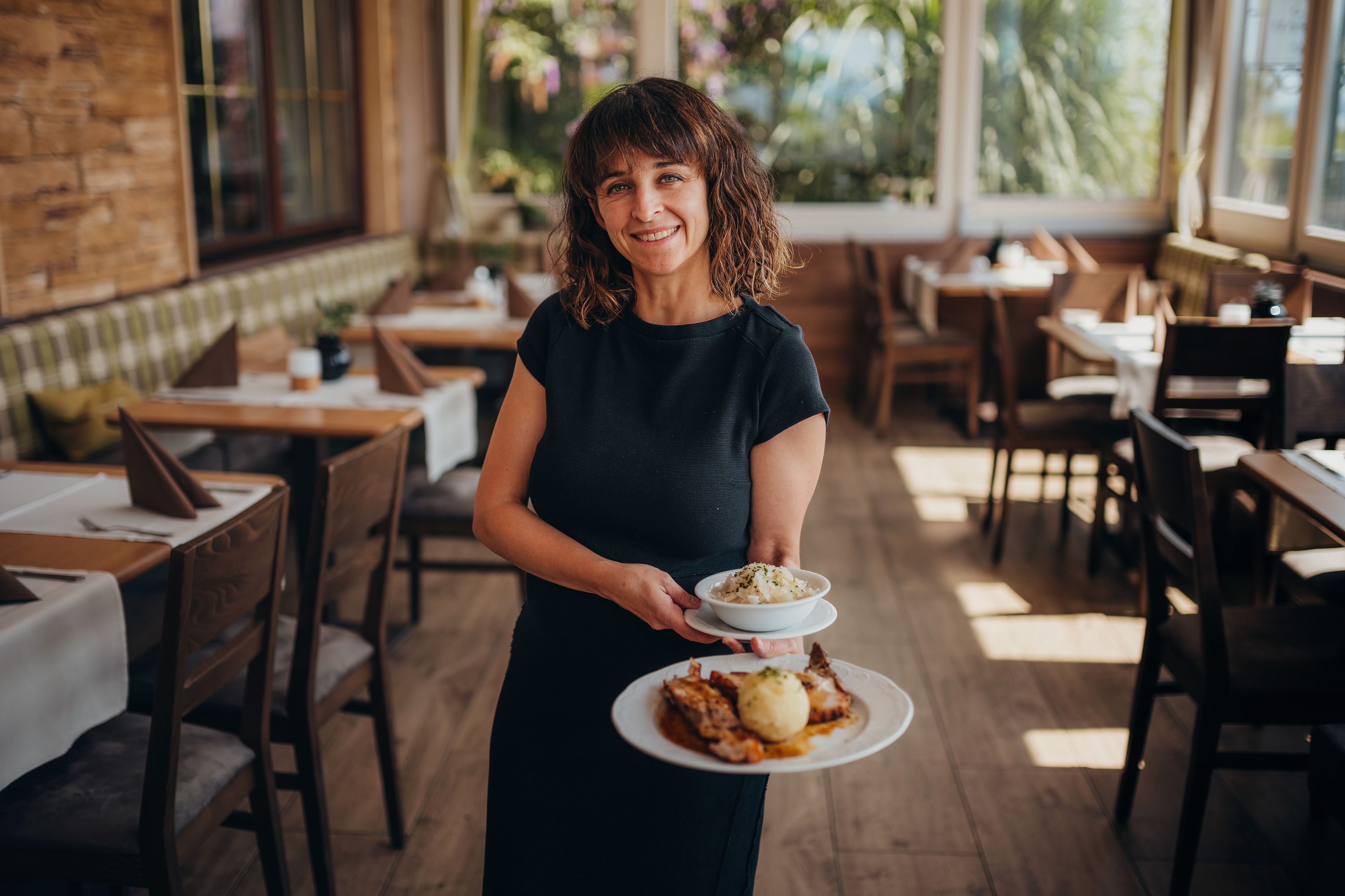 Frau serviert Essen in einem gemütlichen Restaurant mit Holzmöbeln.