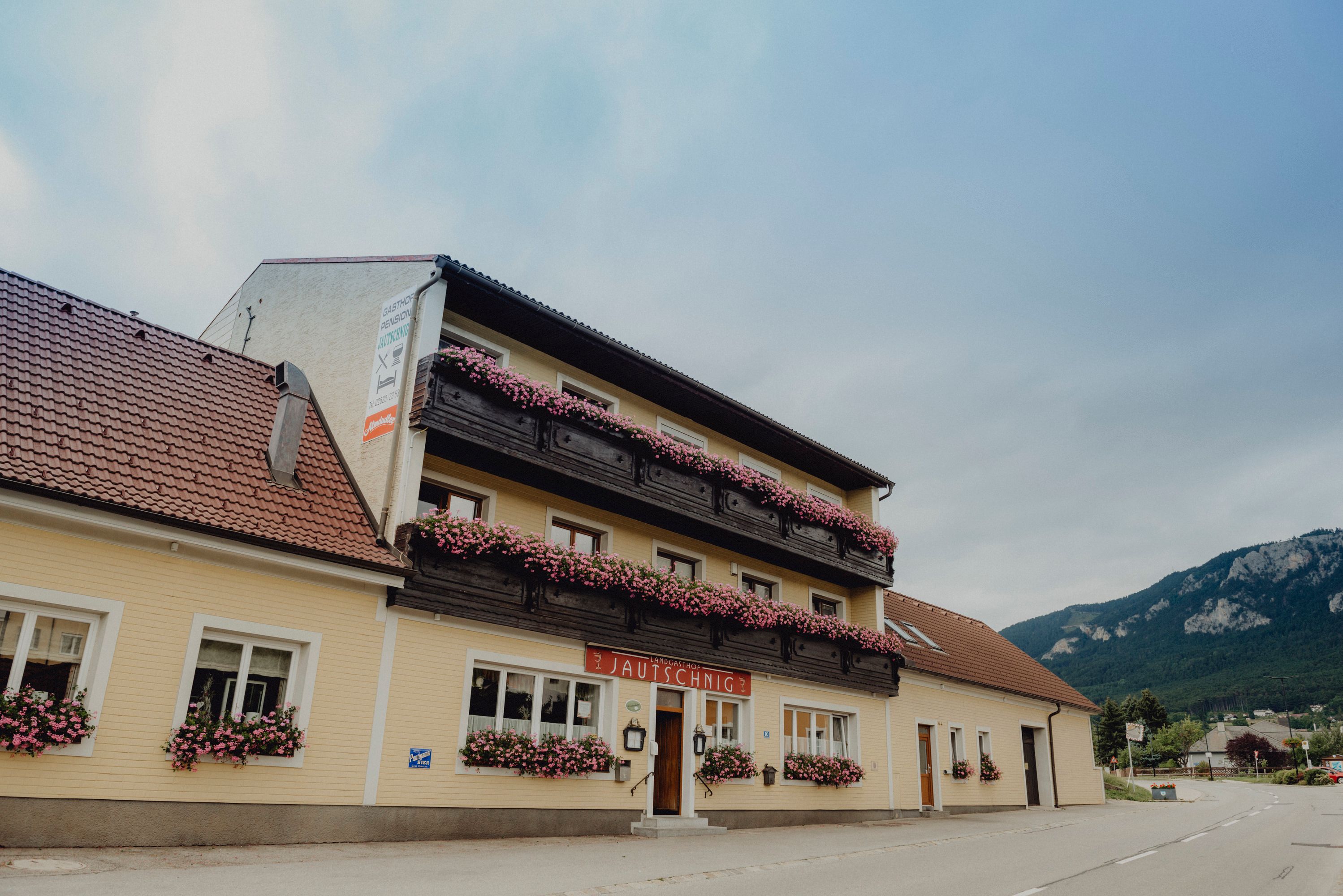 Ein traditioneller Landgasthof mit Blumen geschmückten Balkonen vor einer Bergkulisse.