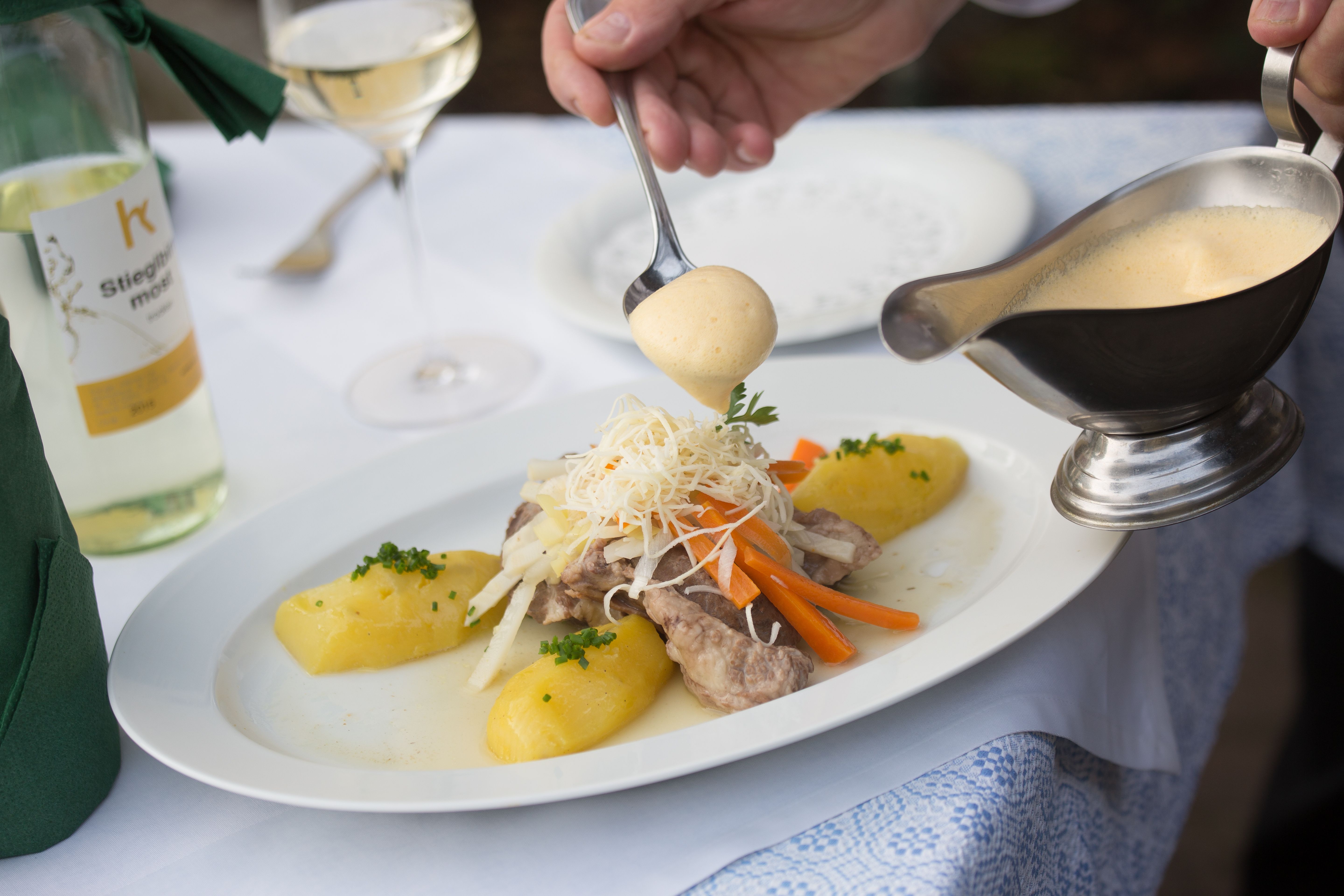 Ein Teller mit Fleisch, Gemüse und Kartoffeln wird mit Sauce übergossen.