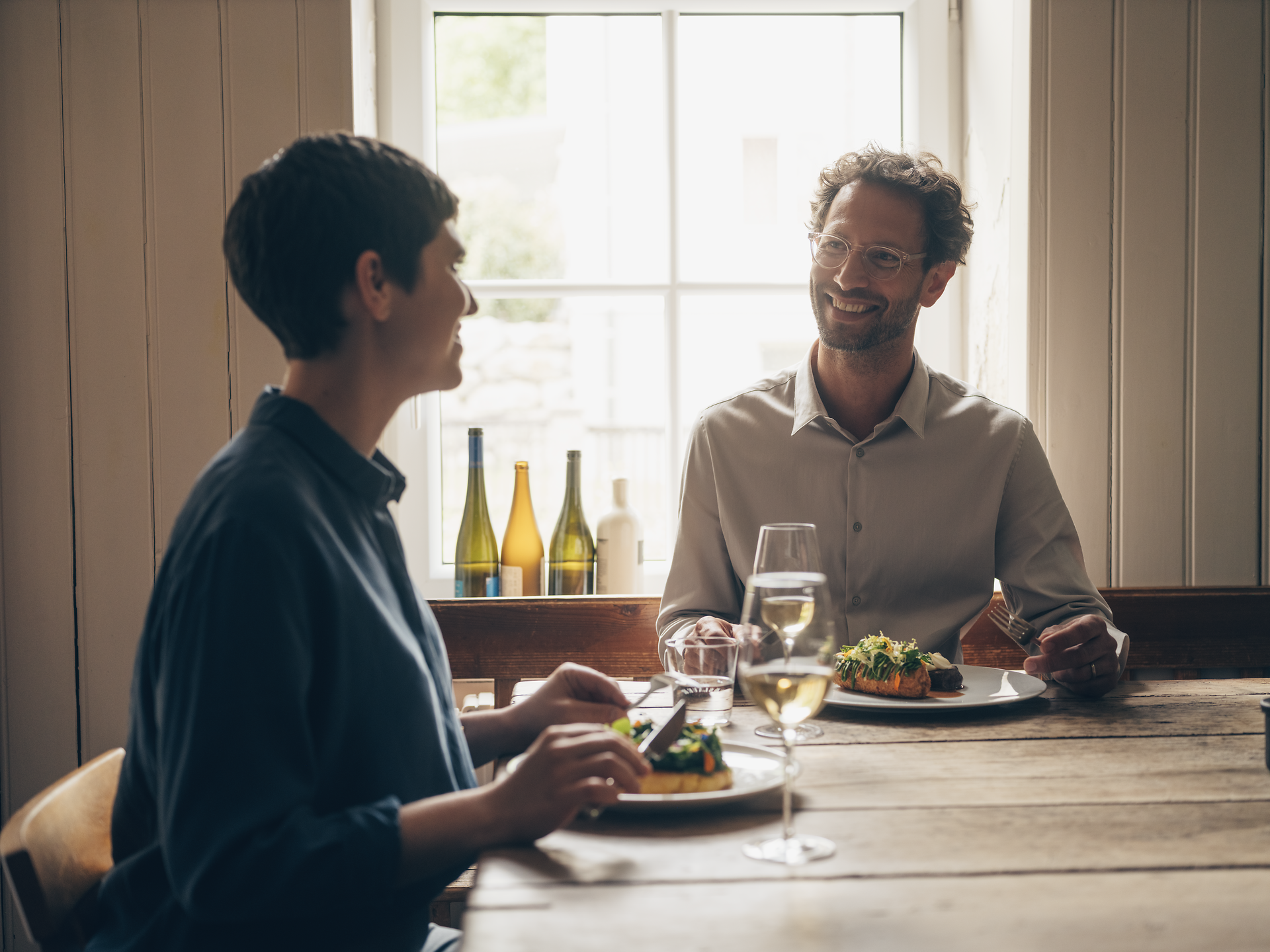 In einem gemütlichen Wirtshaus genießen zwei Gäste ein köstliches kulinarisches Erlebnis. Die liebevoll angerichteten Gerichte, darunter zartes Bio-Rind und frische Wildkräuter, laden zum Schlemmen und Verweilen ein. Die Atmosphäre ist entspannt und einladend, perfekt für einen genussvollen Abend.