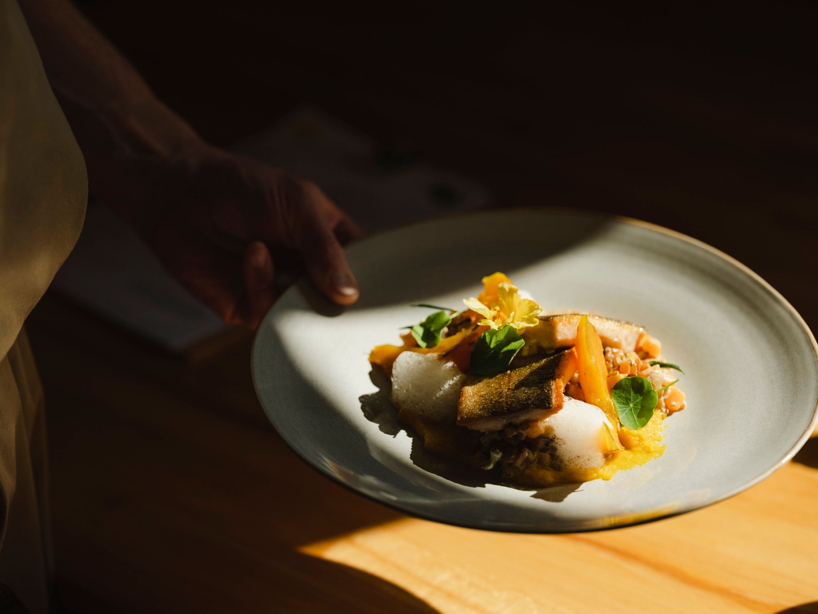 Gourmetgericht mit Fisch, Risotto und Kürbis auf grauem Teller.