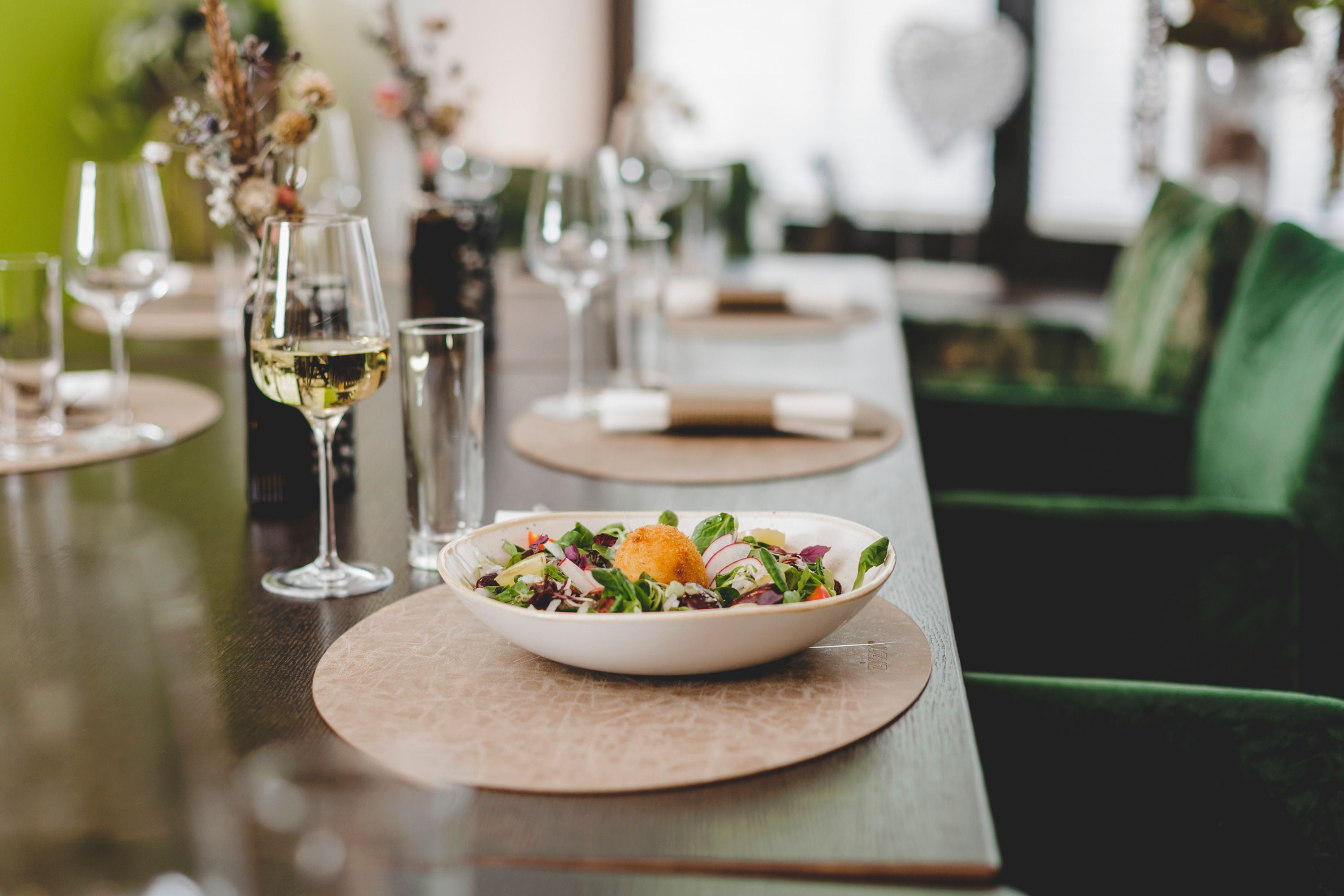 Ein gedeckter Tisch mit einem Salatteller und einem Glas Weißwein.