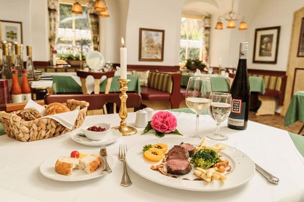 Elegantes Restaurant mit gedecktem Tisch, Kerze, Weinflasche und Teller mit Fleischgericht.