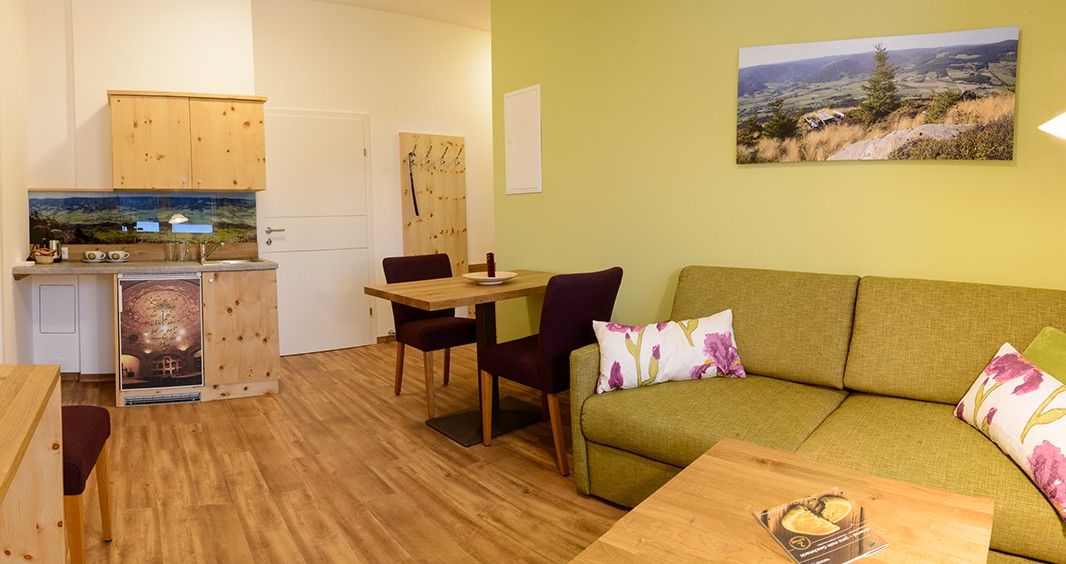 Gemütliches Zimmer mit grüner Couch, Holzmöbeln und Landschaftsfoto an der Wand.