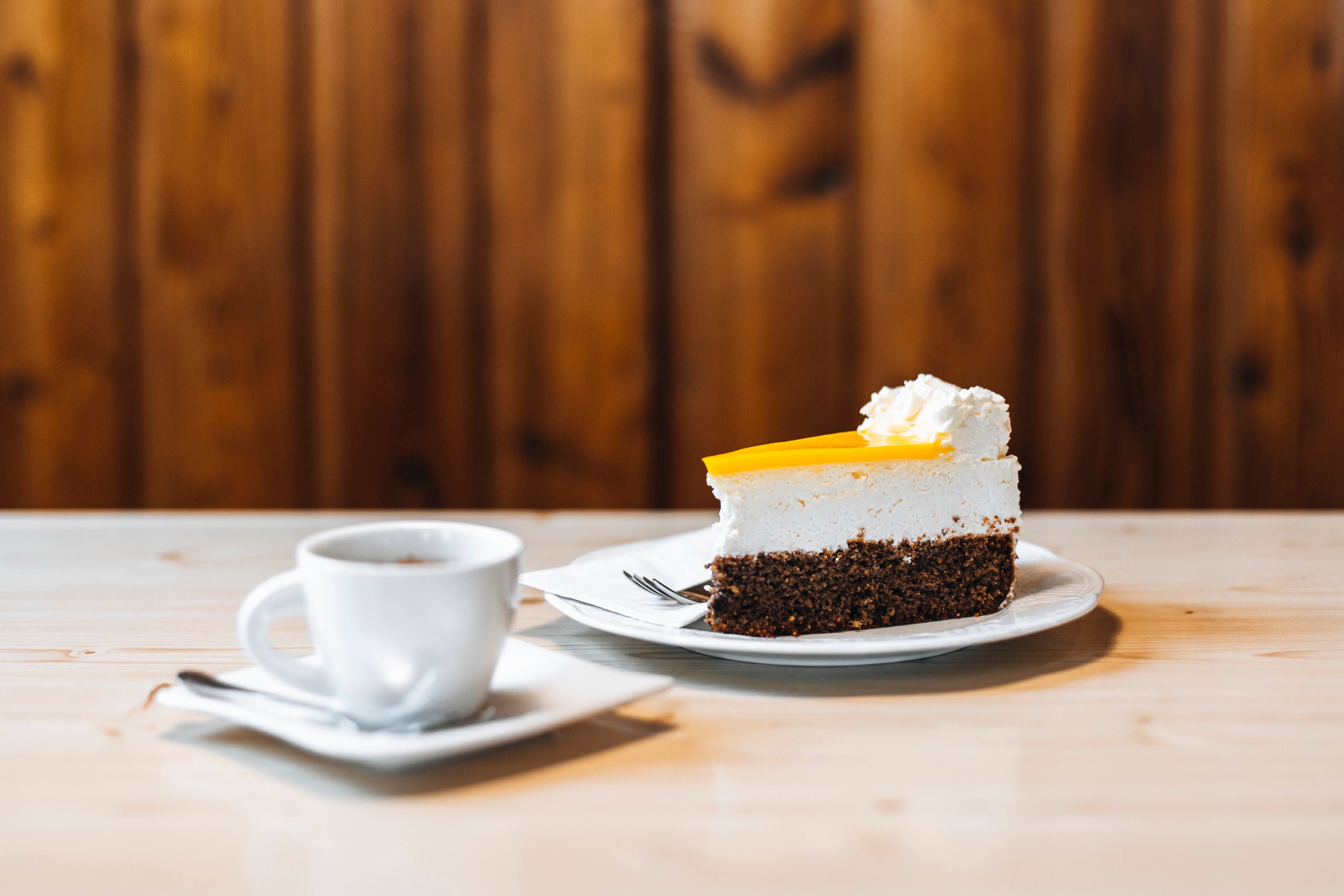 Stück Kuchen mit Sahne und Tasse Kaffee auf Holztisch.
