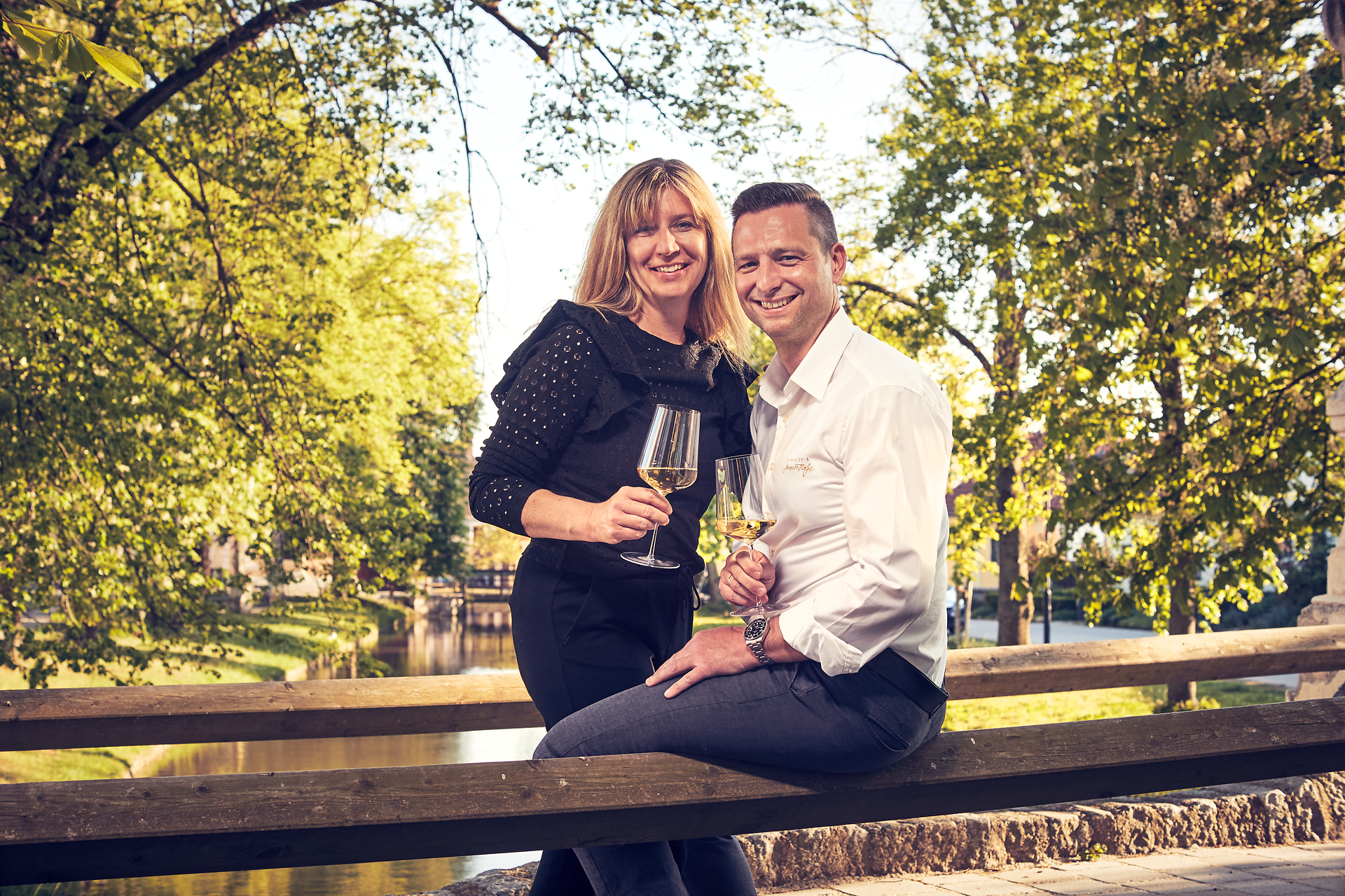 Inmitten eines malerischen Gartens genießen die Wirtsleute ein Glas Wein und die warmen Sonnenstrahlen. Die üppigen Bäume und das sanfte Plätschern des Wassers schaffen eine einladende Atmosphäre, die zum Verweilen einlädt. Hier wird die Wirtshauskultur lebendig und verspricht unvergessliche Momente.