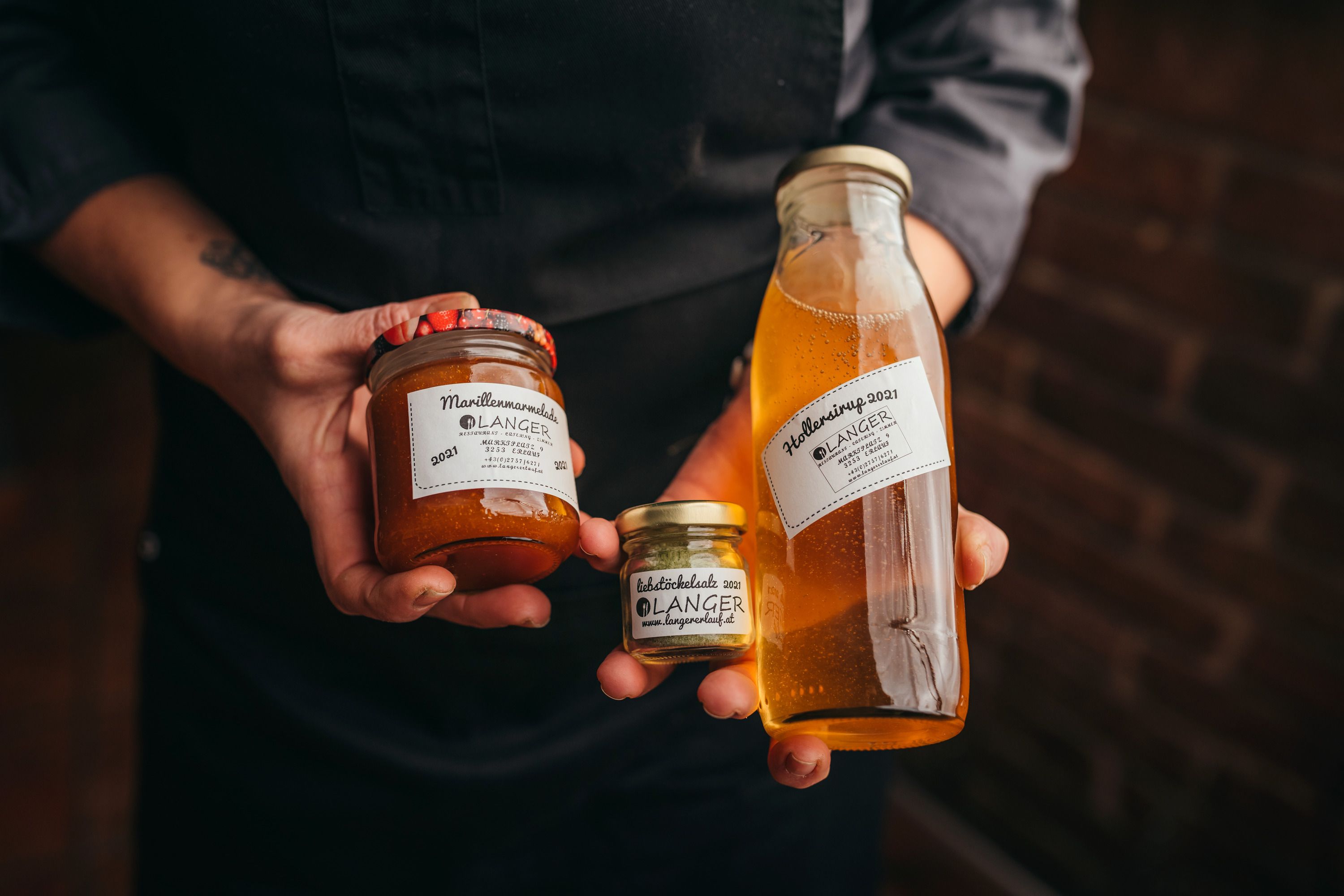 Person hält Gläser mit Marillenmarmelade und Hollersirup von Langer.