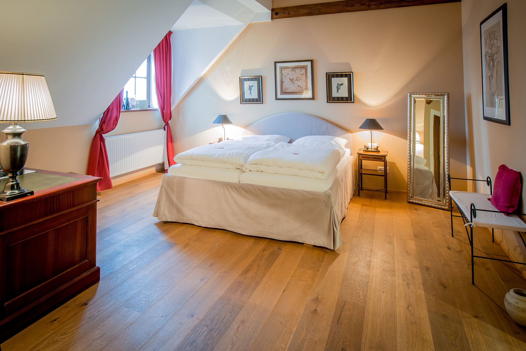 Ein gemütliches Doppelzimmer mit Holzboden, einem großen Bett, roten Vorhängen und stilvollen Dekorationen.