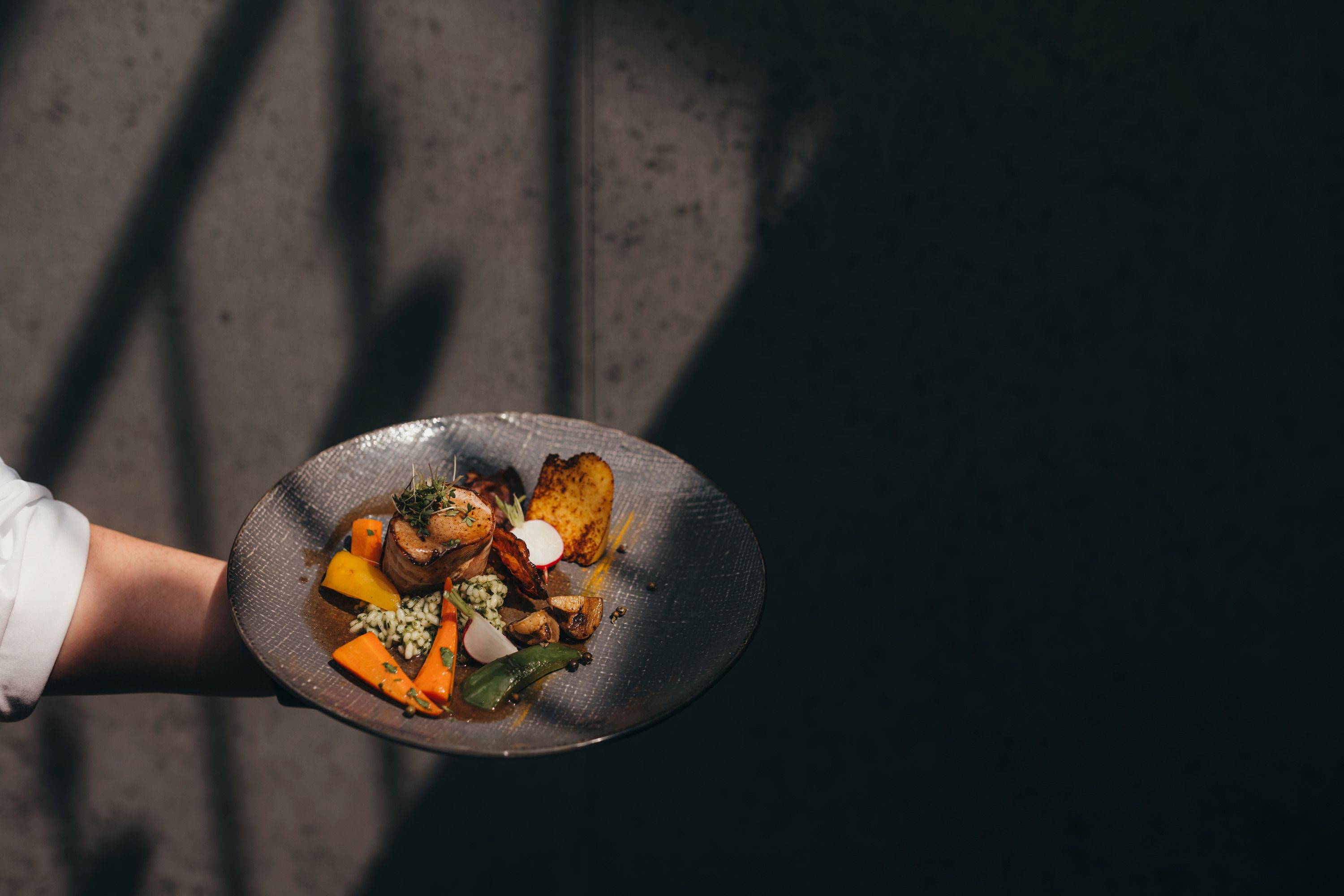 Ein Teller mit modern interpretierter Waldviertler Küche, präsentiert von einer Hand vor einem dunklen Hintergrund.