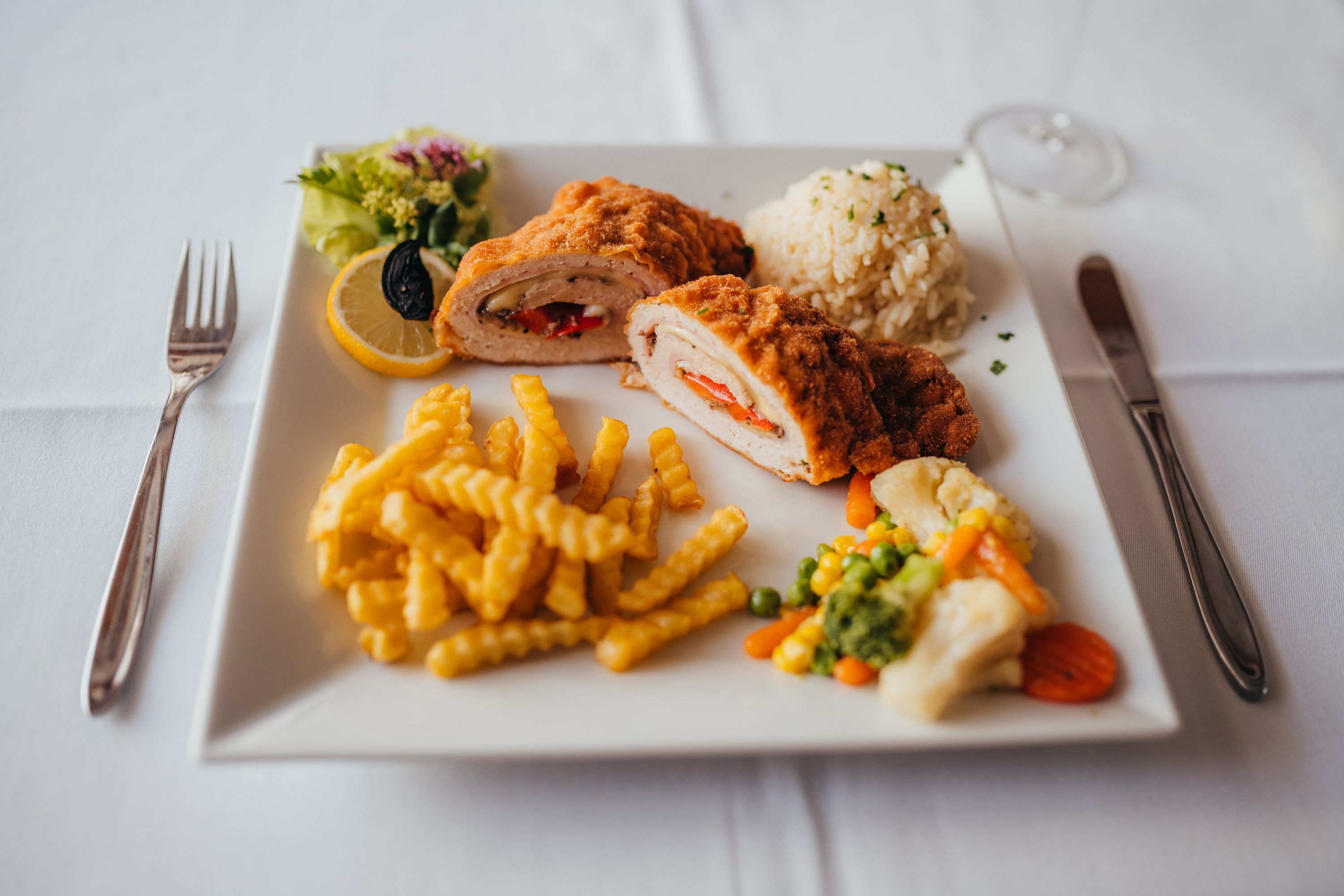 Gebackenes Hähnchen mit Pommes, Reis und Gemüse auf weißem Teller.