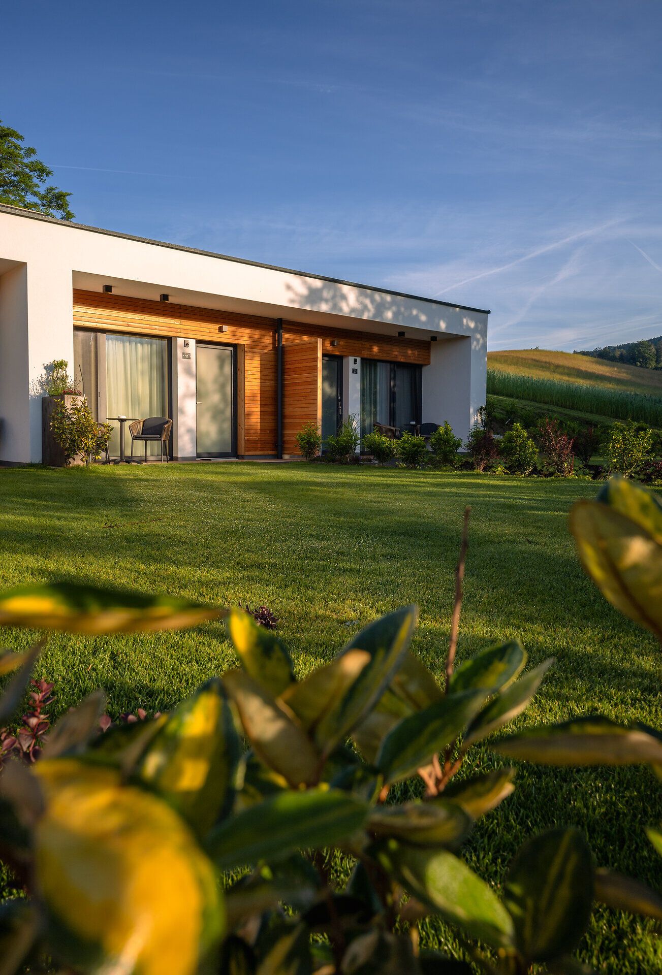 Inmitten einer malerischen Landschaft strahlt das moderne Haus mit seinen klaren Linien und warmen Holzelementen eine einladende Atmosphäre aus. Der gepflegte Garten, umgeben von sanften Hügeln, lädt dazu ein, die frische Bergluft zu genießen und die Ruhe der Natur zu erleben.