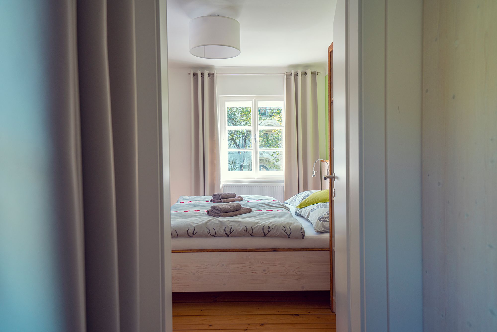 Ein gemütliches Gästezimmer mit Doppelbett, Bettwäsche mit Hirschmotiven und gefalteten Handtüchern auf dem Bett, durch eine offene Tür gesehen.