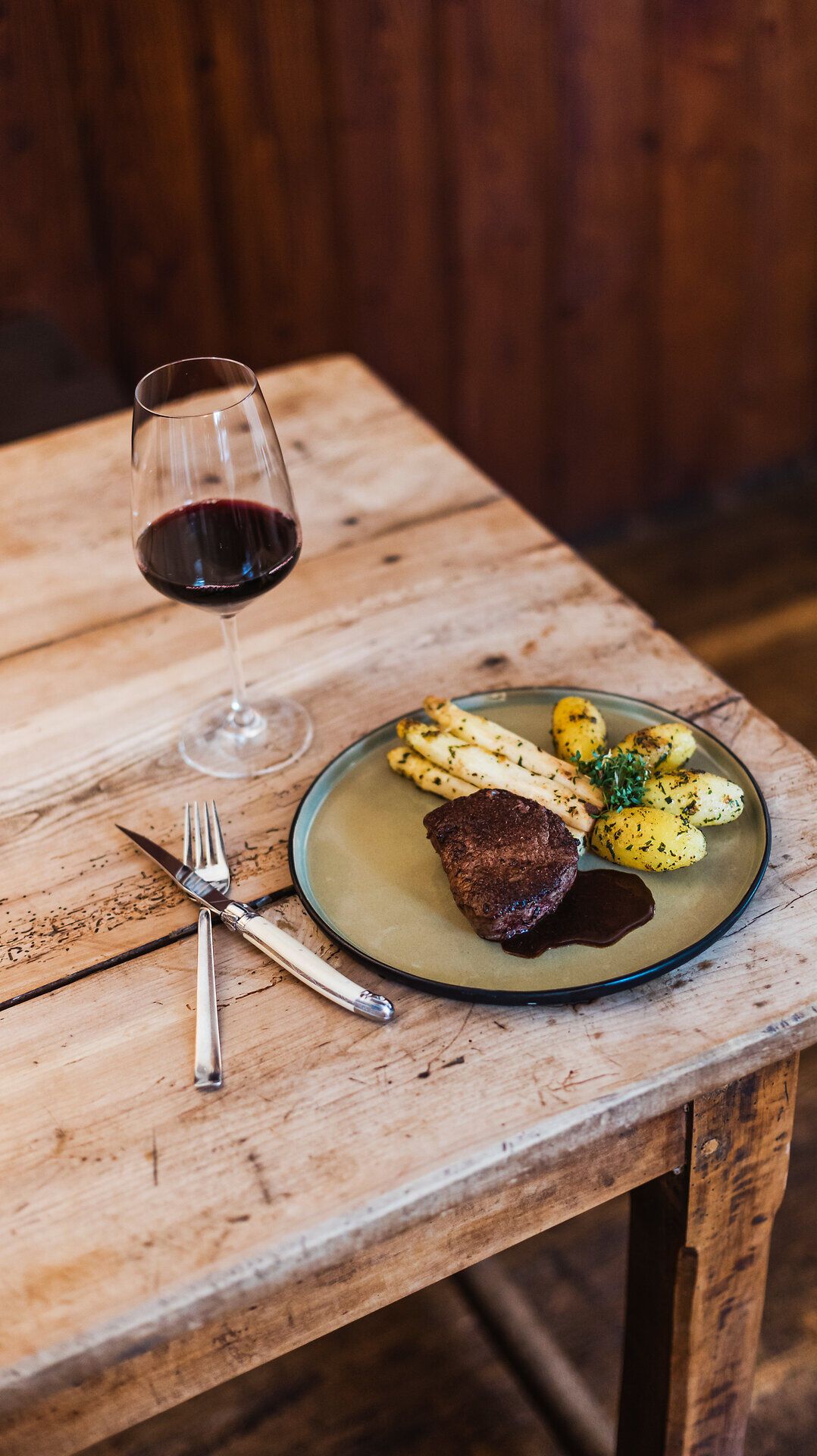 Ein köstliches Rinderfilet, perfekt zubereitet, liegt auf dem Teller, umgeben von zarten Spargelstangen und aromatischen Petersilienkartoffeln. Ein Glas tiefroter Most ergänzt das kulinarische Erlebnis und lädt dazu ein, die regionale Wirtshauskultur in vollen Zügen zu genießen.