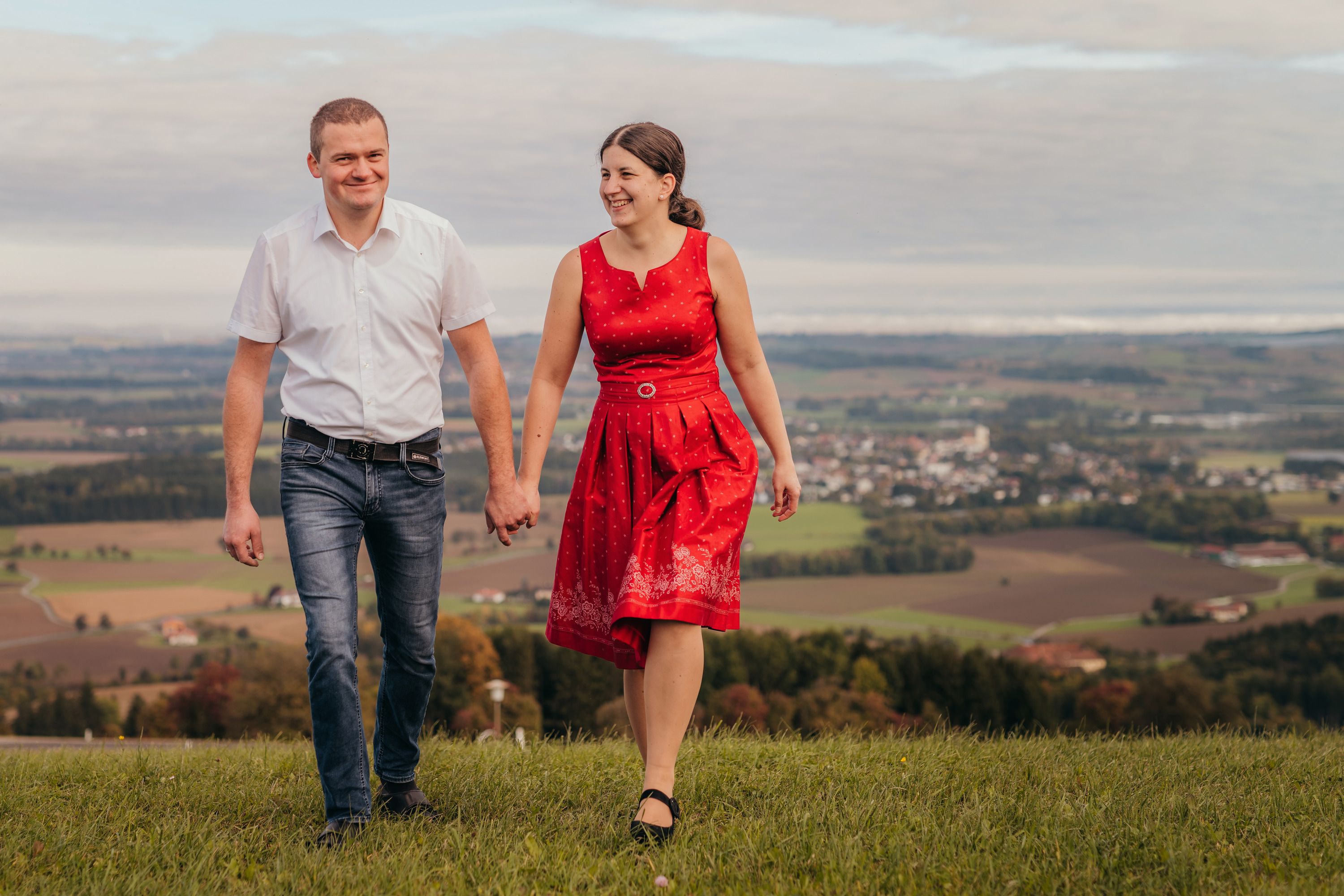 Ein Paar hält Händchen und geht über eine Wiese mit einer Landschaft im Hintergrund.