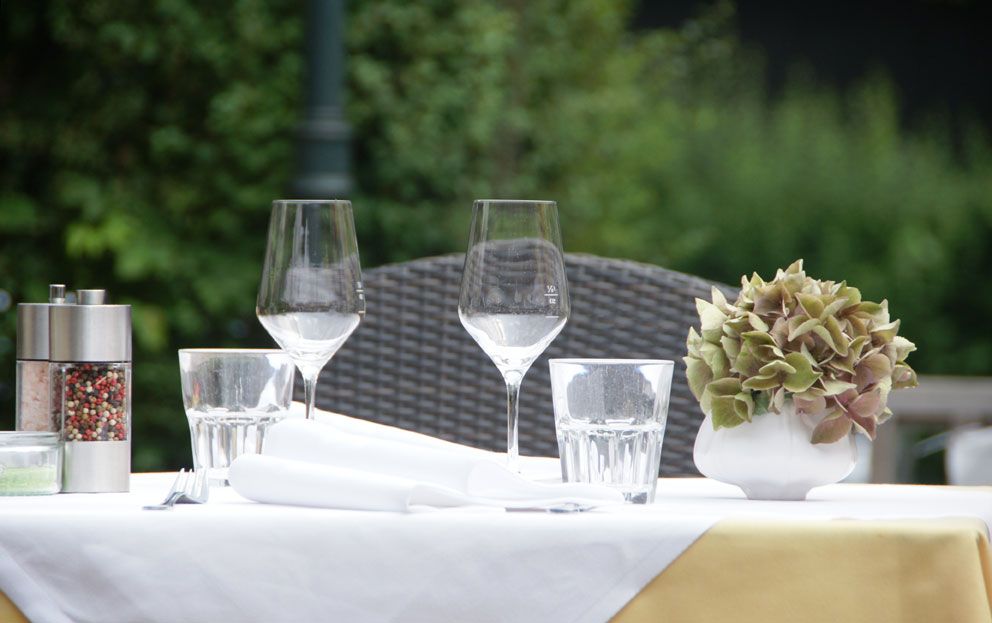 Gedeckter Tisch im Freien mit Weingläsern, Wassergläsern, Pfeffermühle und Blumendekoration.