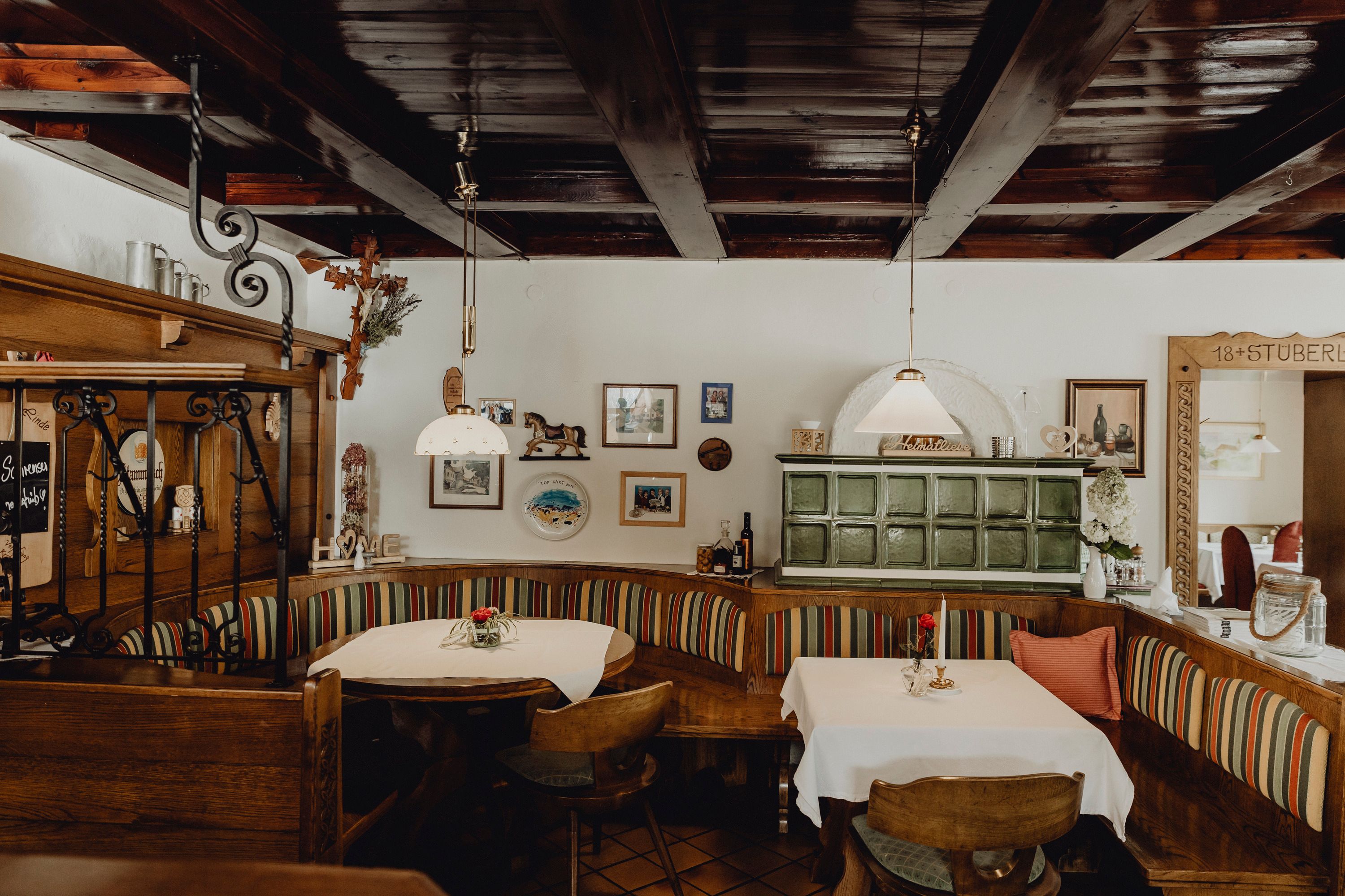 Gemütliche Gaststube mit Holzmöbeln, Kachelofen und dekorativen Bildern an der Wand.