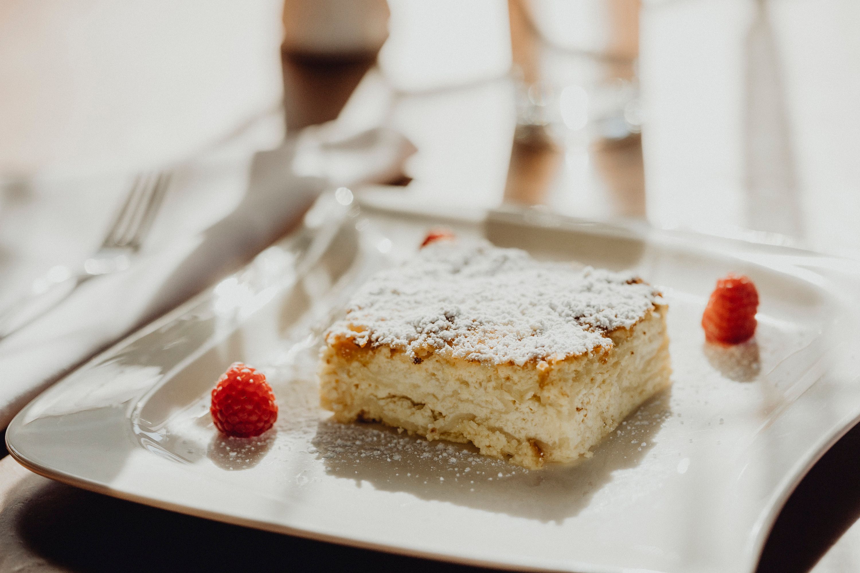 Ein Stück Milchrahmstrudel mit Puderzucker und Himbeeren auf einem weißen Teller.