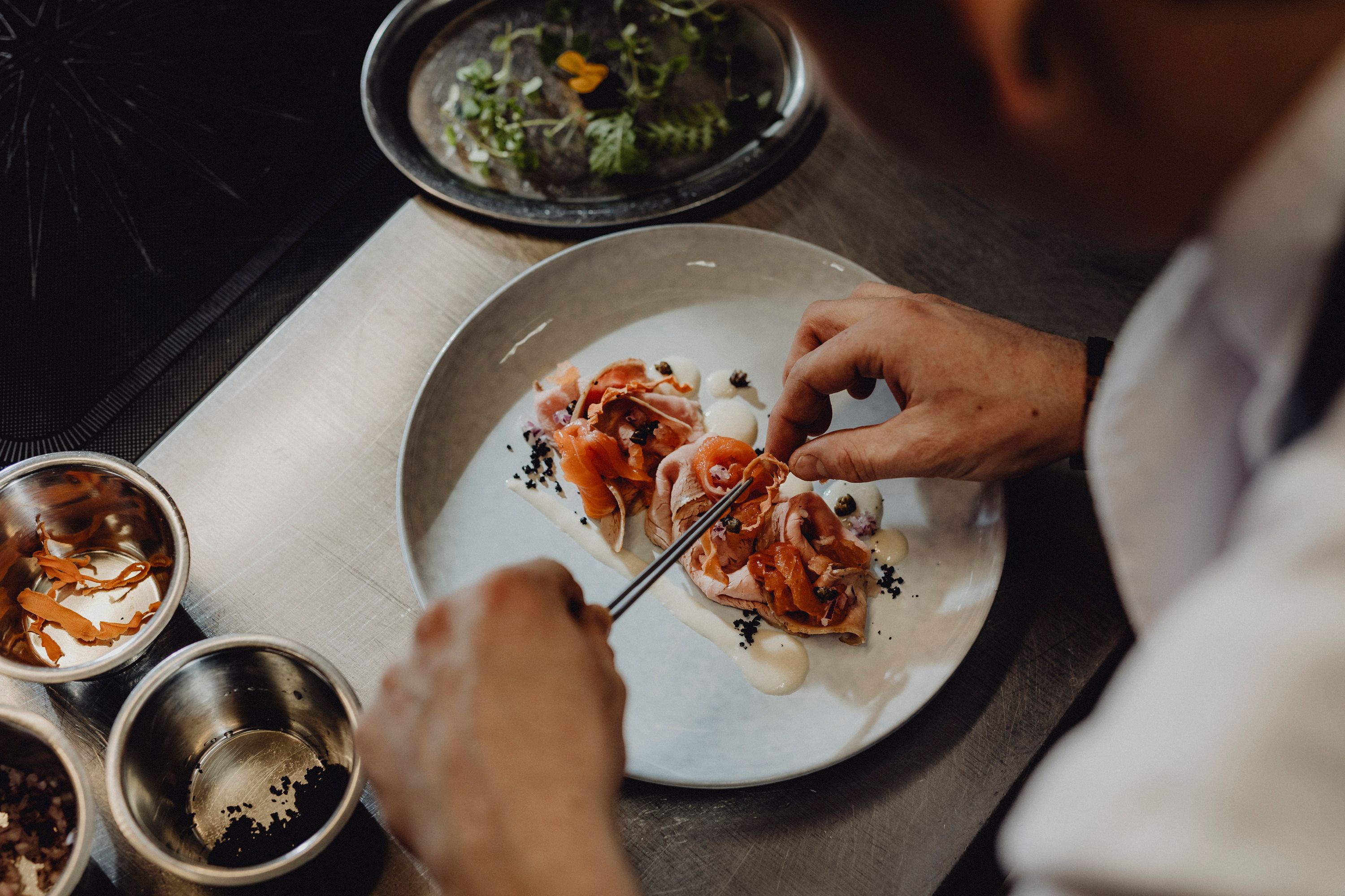 Koch dekoriert ein Gericht mit Lachs und Gemüse auf einem Teller.