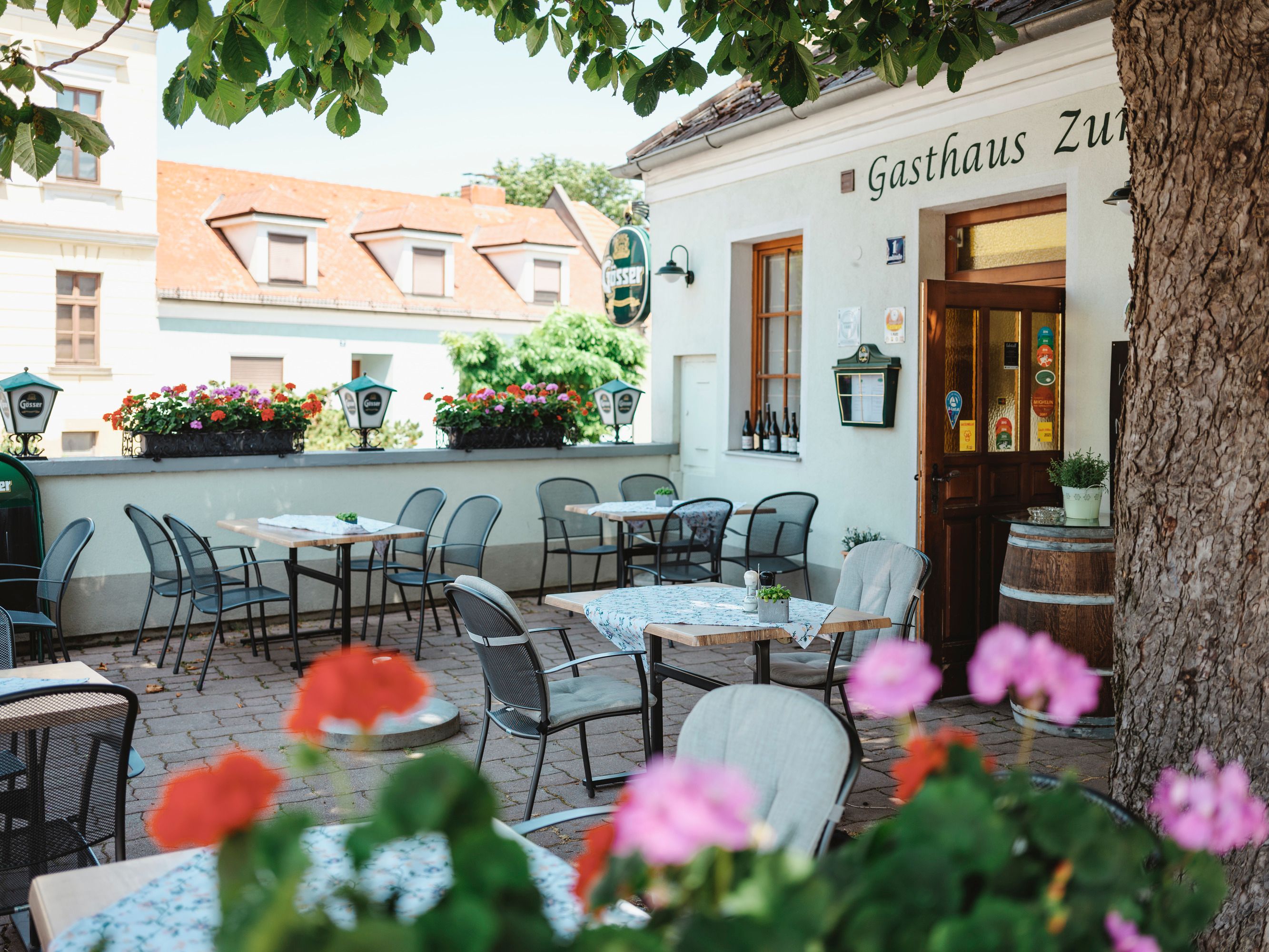 Schattiger Gastgarten mit Tischen und Stühlen vor einem Gasthaus.