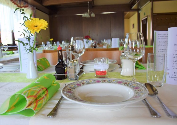 Festlich gedeckter Tisch in einem Saal mit Blumen, Geschirr und Gläsern.