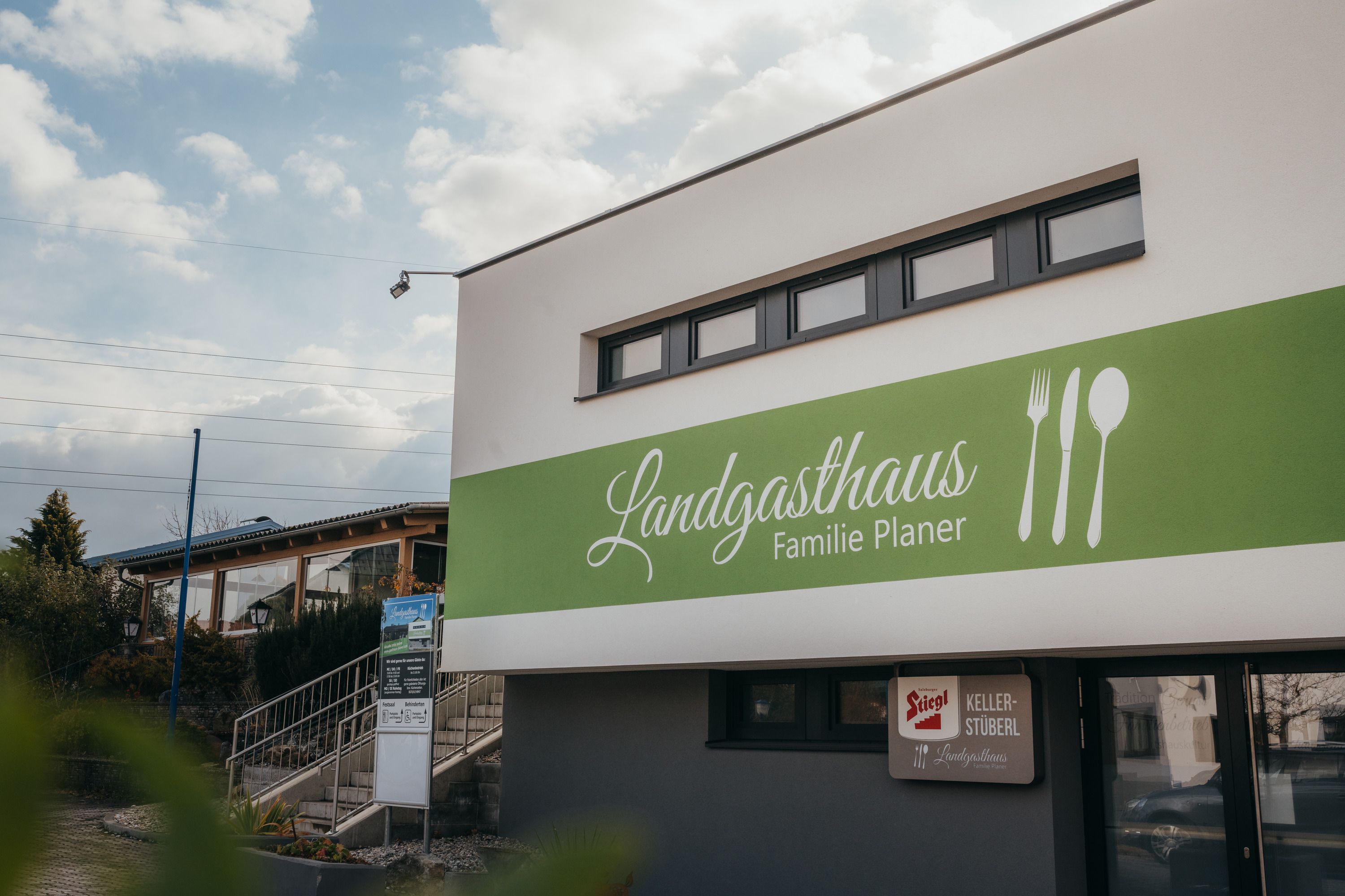 Außenansicht des Landgasthauses Familie Planer mit grünem Schild und Bestecksymbolen.