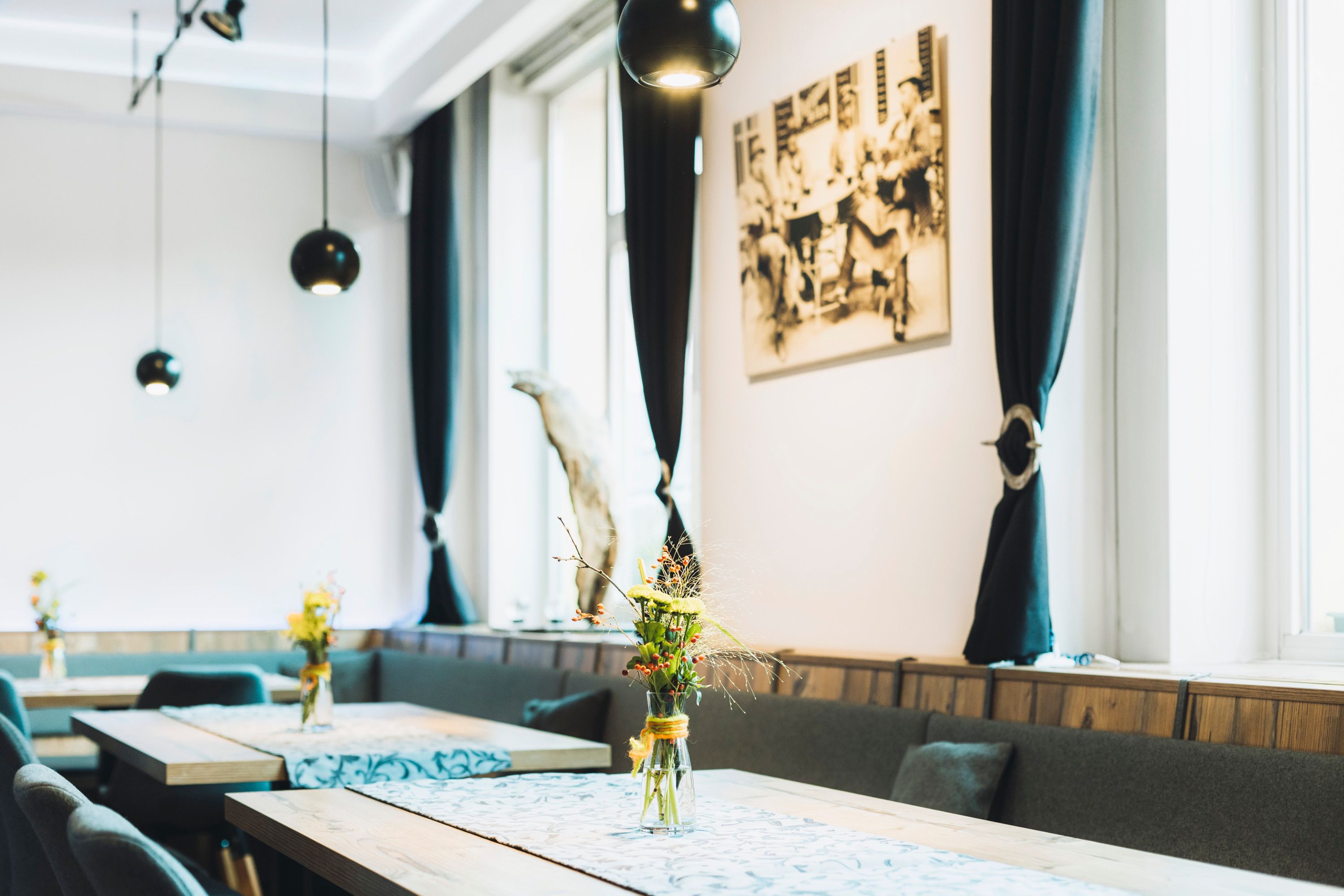 Innenansicht eines stilvollen Cafés mit Holztischen, Blumenvasen und schwarzen Vorhängen.