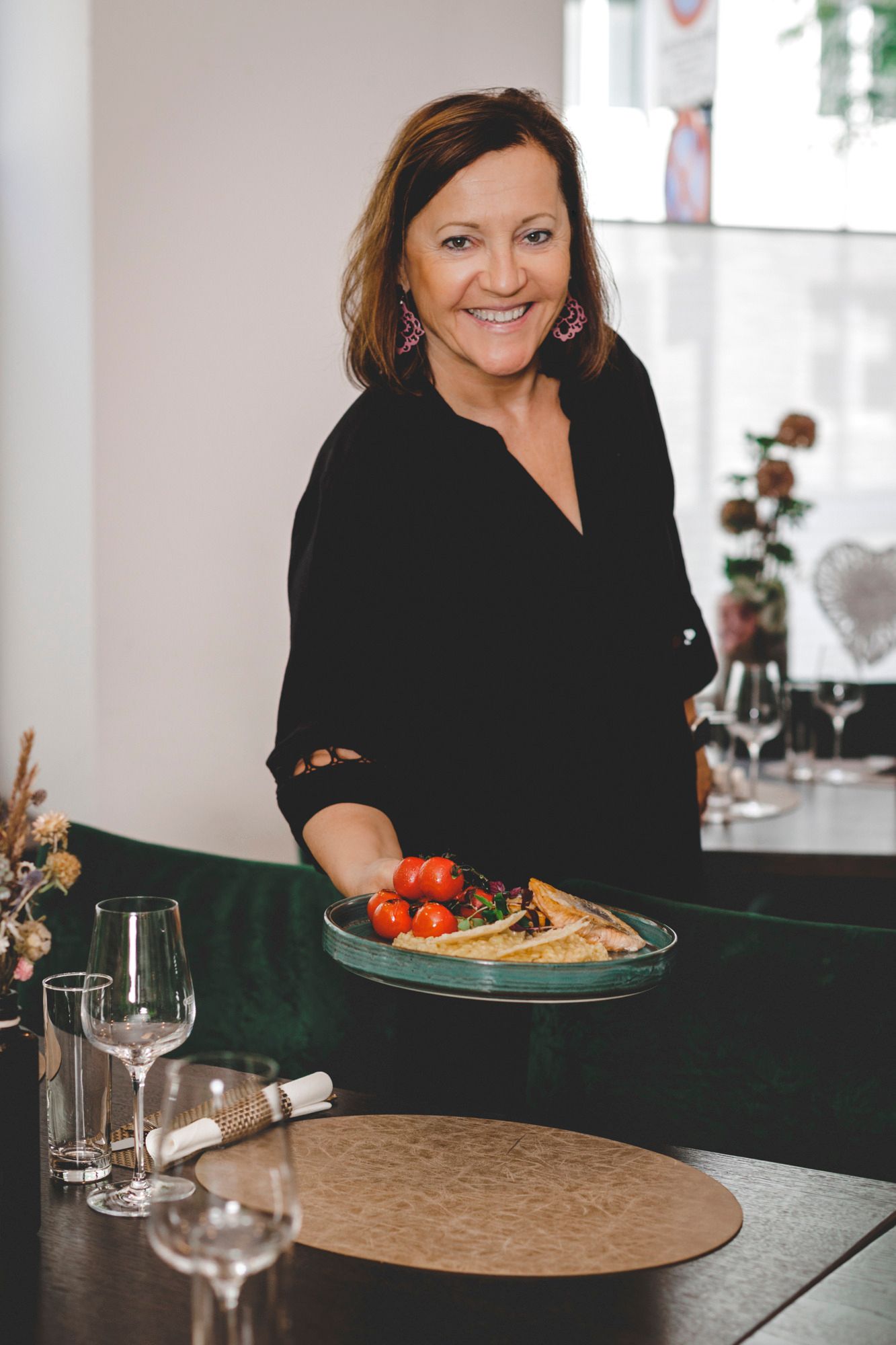 Eine Frau in schwarzer Kleidung serviert ein Gericht mit Tomaten und Fisch in einem Restaurant.