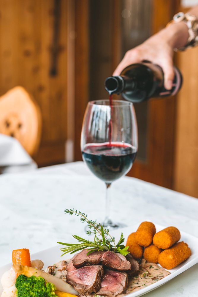 Fleischgericht mit Kroketten und Rotwein auf weißem Tisch.