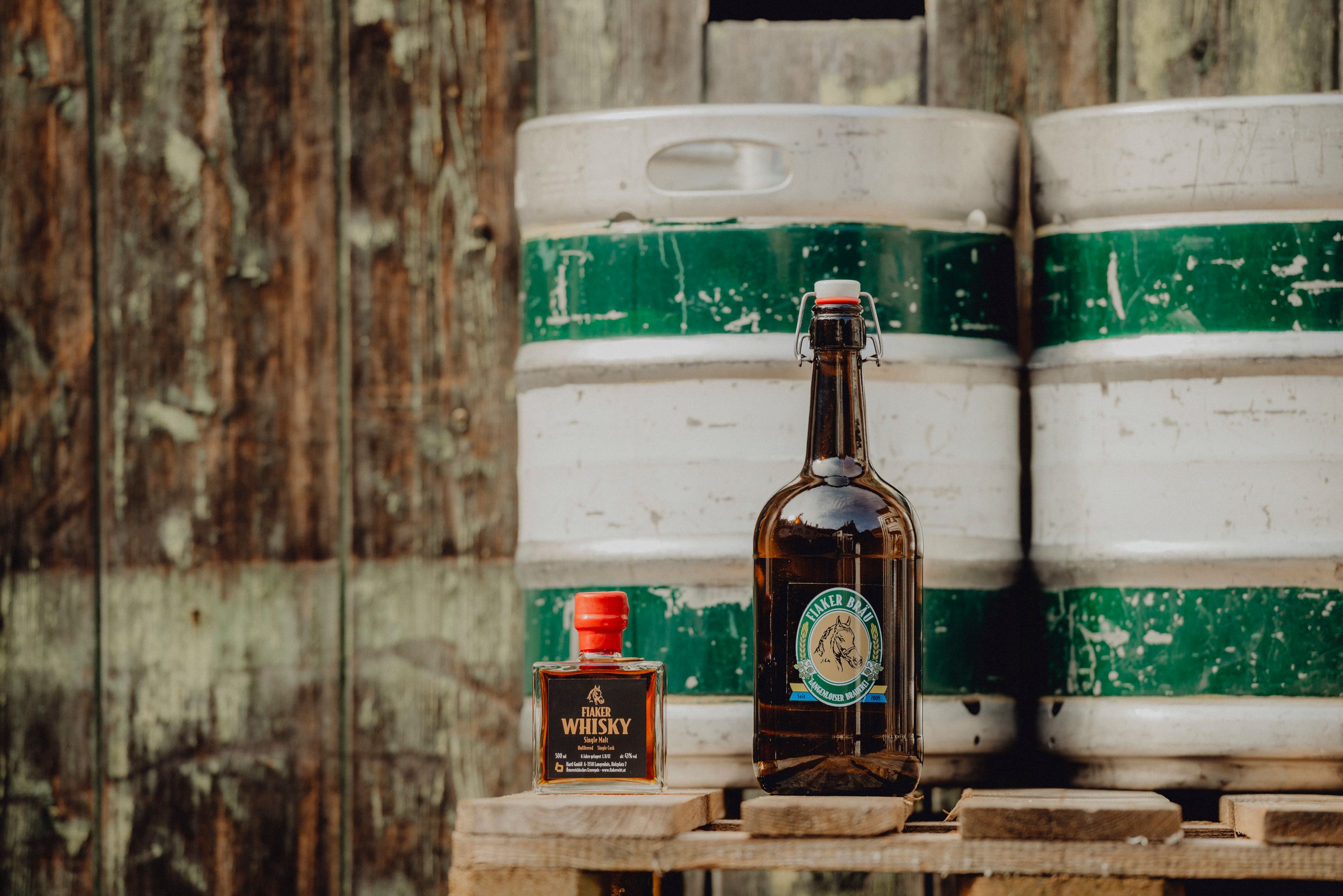 Flasche Fiakerbräu und Fiaker Whisky vor Holzfass.