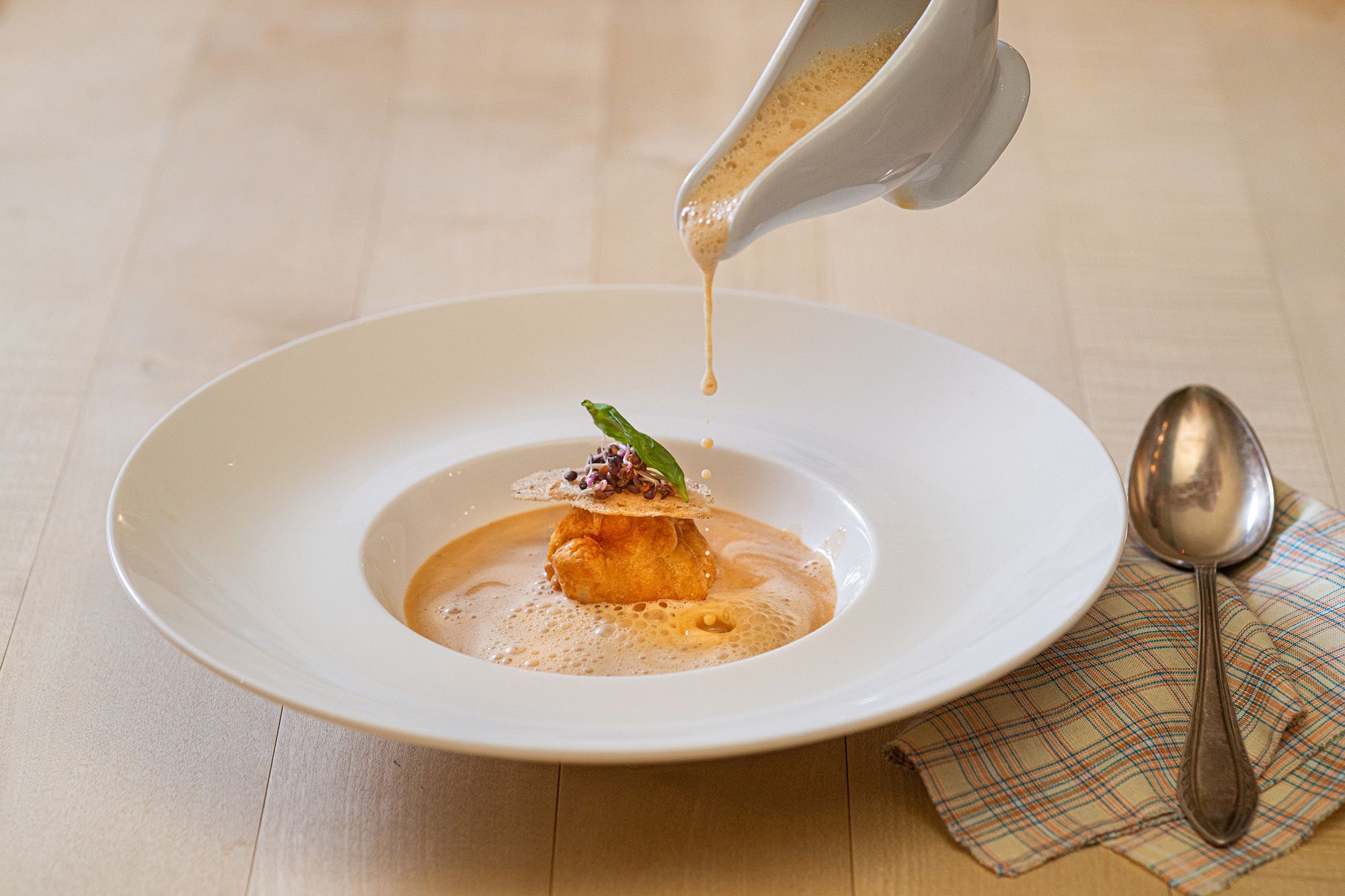 Krebssuppe wird in einen Teller gegossen, dekoriert mit einer Teigkugel und Kräutern.