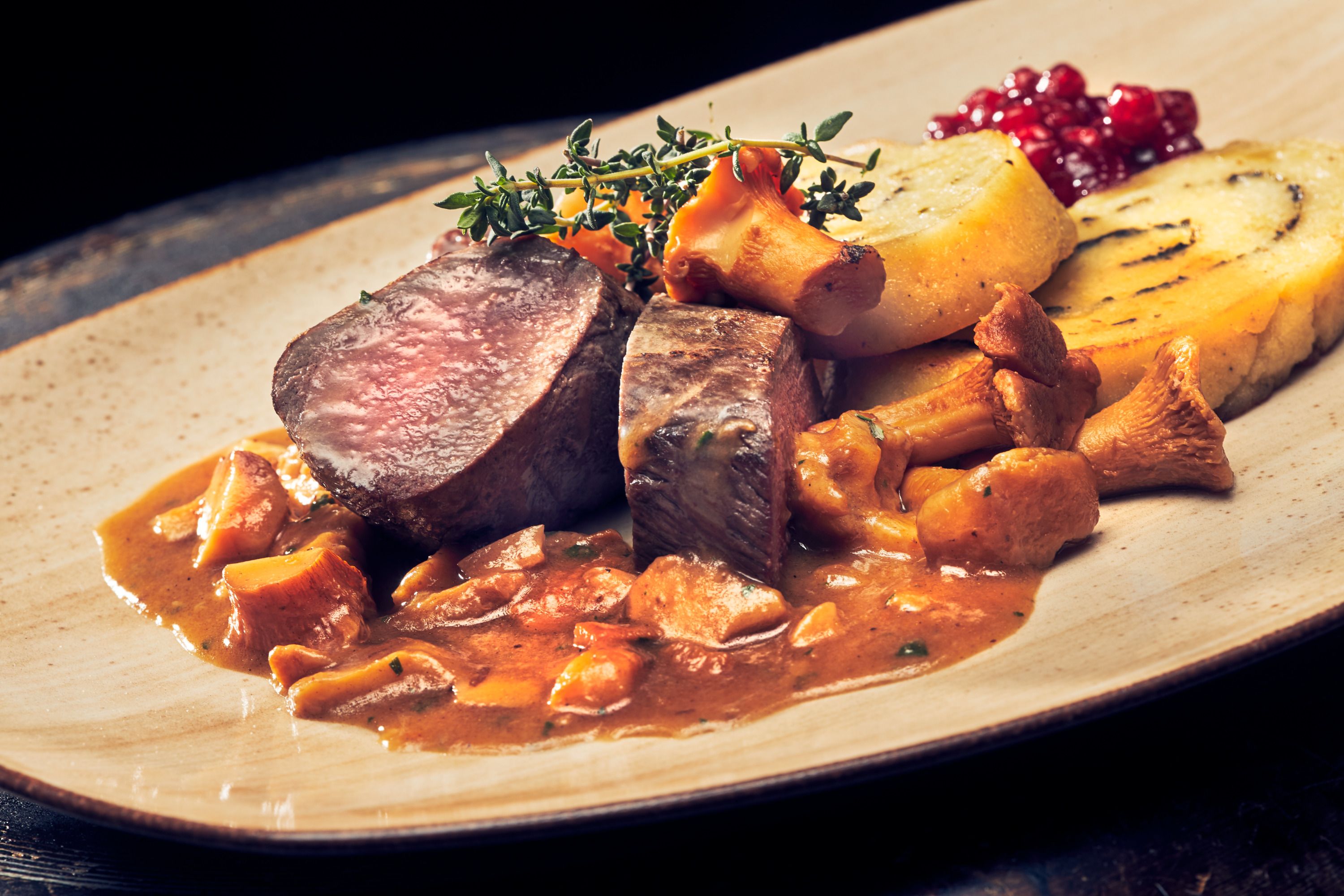 Rehrücken mit Eierschwammerlsauce und Erdäpfel-Kräuterroulade auf einem Teller.