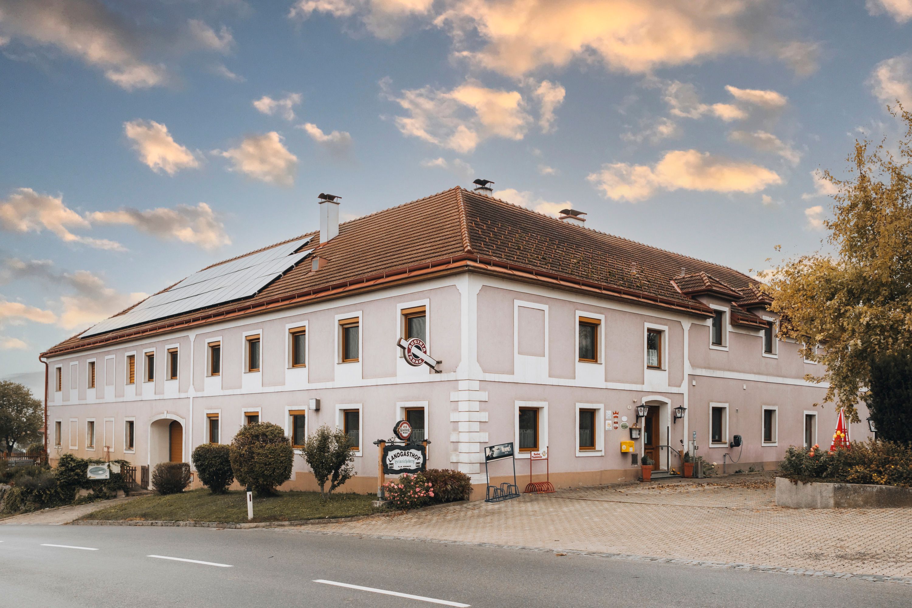 Ein traditioneller Landgasthof mit Solarpanelen auf dem Dach und einem Schild vor dem Eingang, unter einem bewölkten Himmel.
