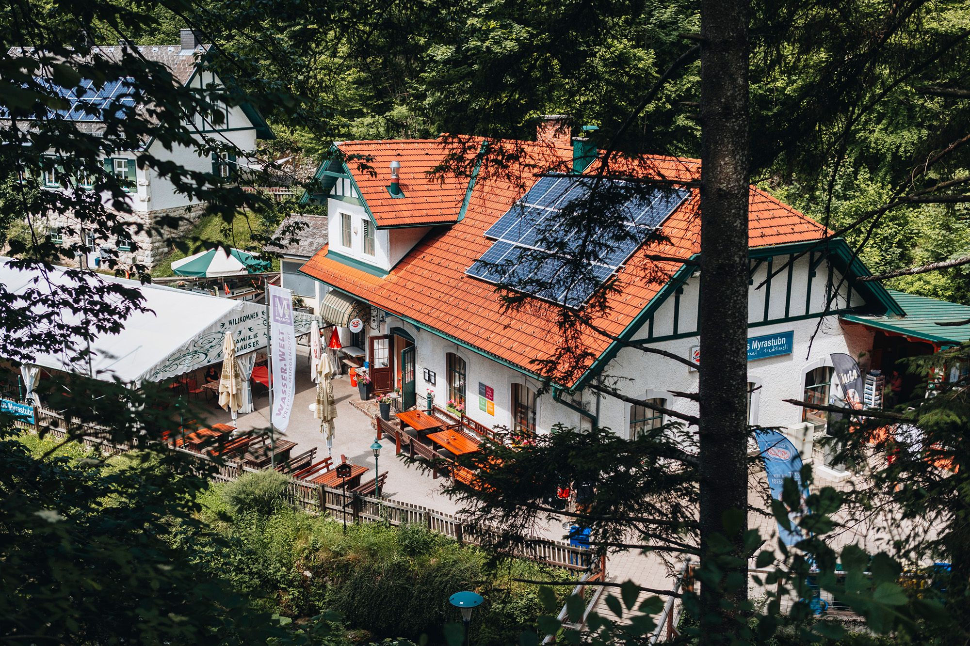Ein traditionelles Gasthaus mit Solarpanelen auf dem Dach, umgeben von Bäumen.